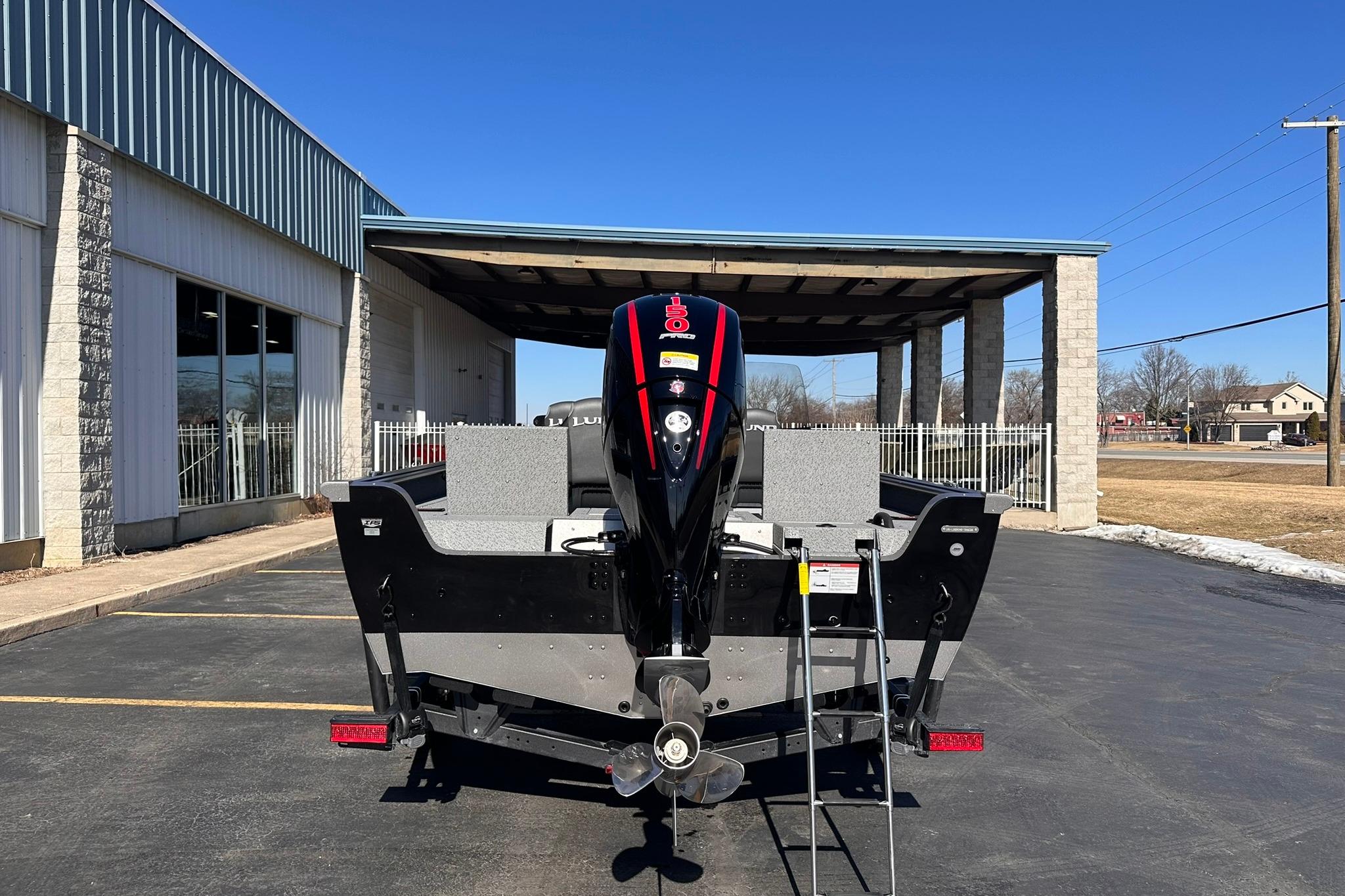 2026 Lund 1875 Impact XS SS boat, rear view with motor, parked outdoors.