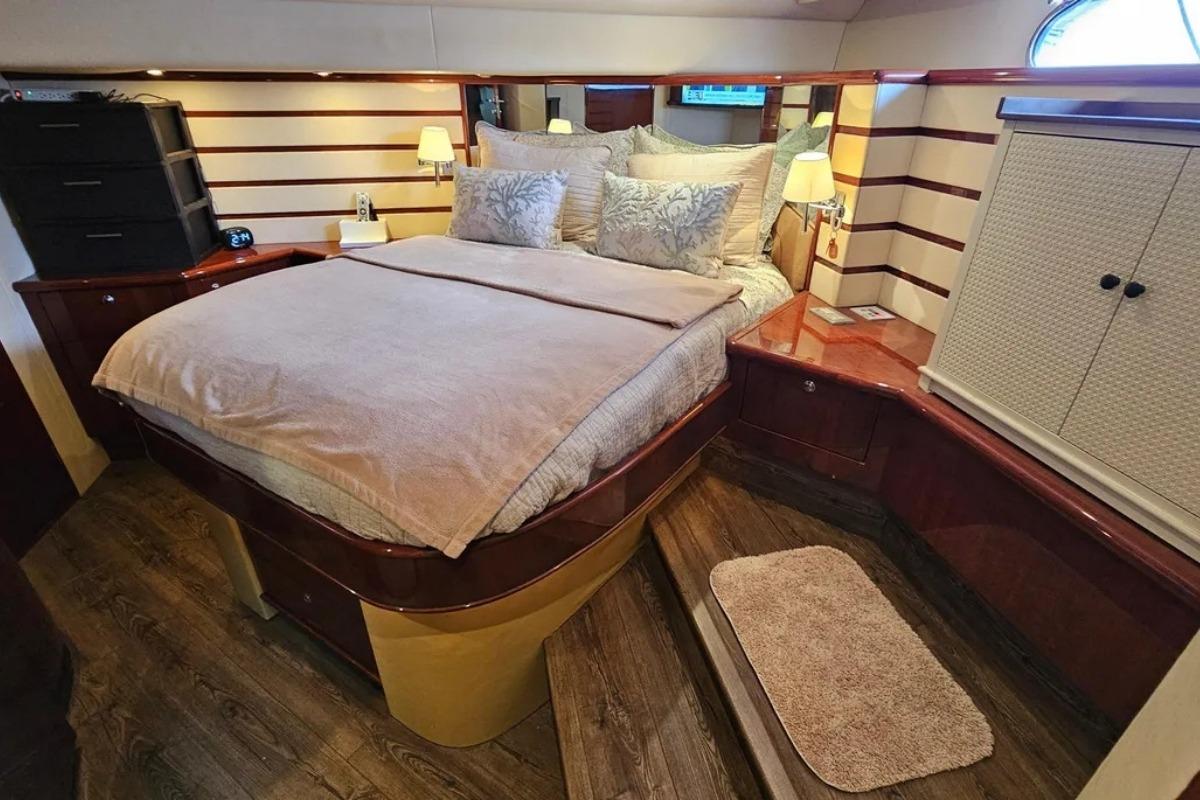 Luxurious 2005 Neptunus 56 Flybridge yacht bedroom with elegant wood finishes and cozy bedding.