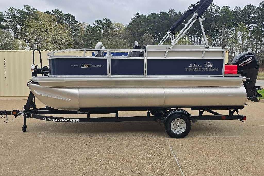 2026 Sun Tracker Bass Buggy 16 XL Select pontoon boat on trailer, parked outdoors.