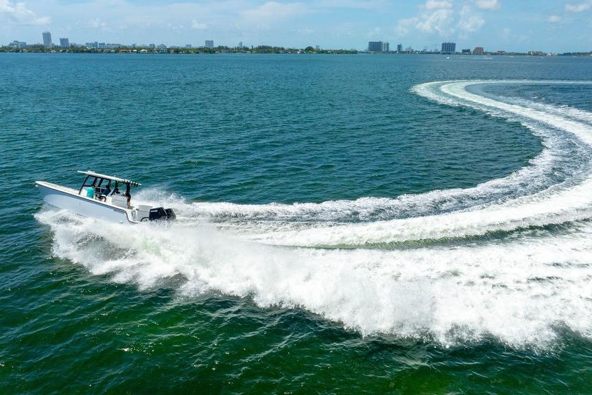 A 2027 Reef Runner 340 boat creating a wake in open water, with city skyline in background.
