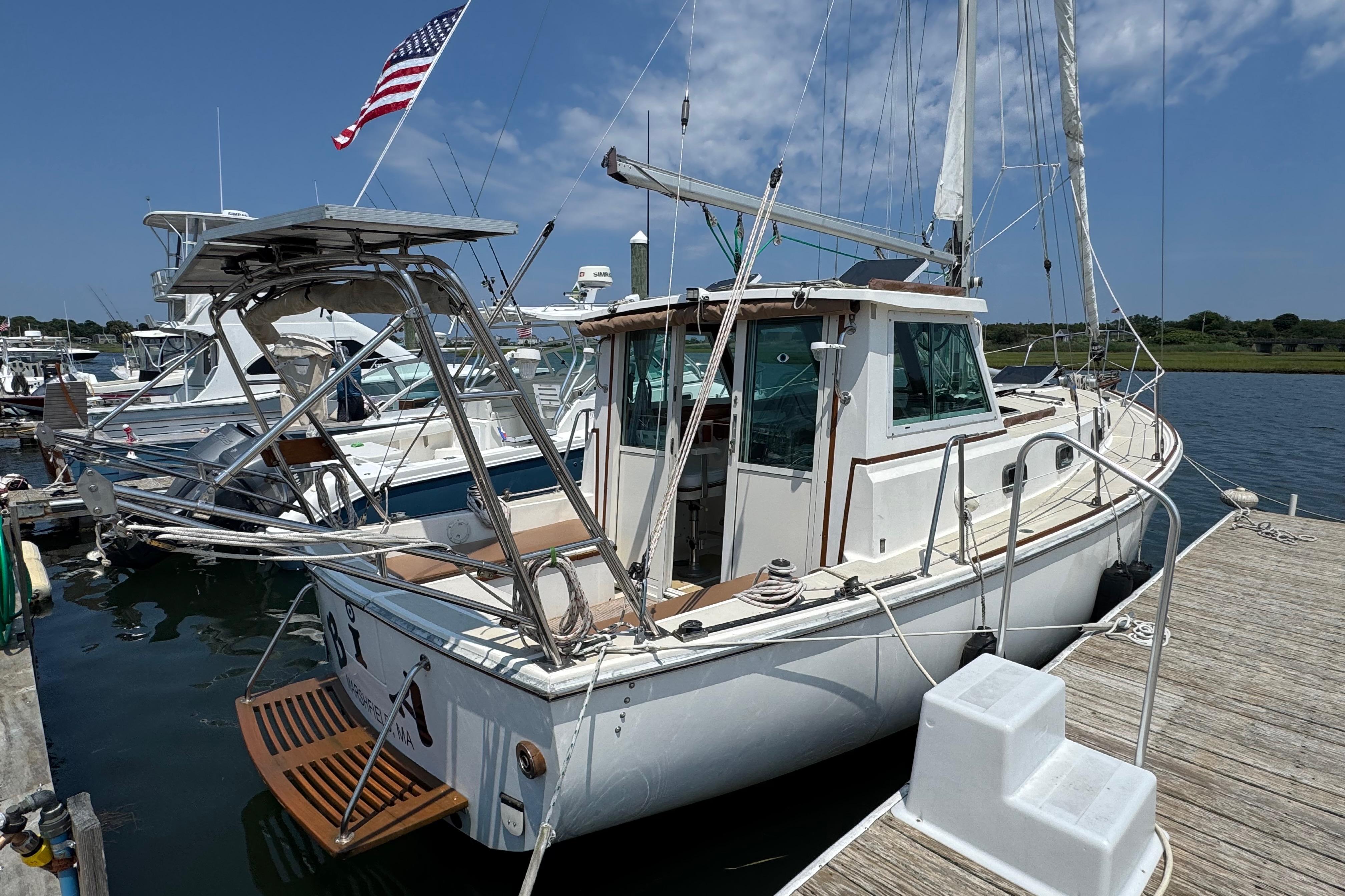 1989 Cape Dory 30 Motorsailer docked, featuring American flag and clear blue sky.
