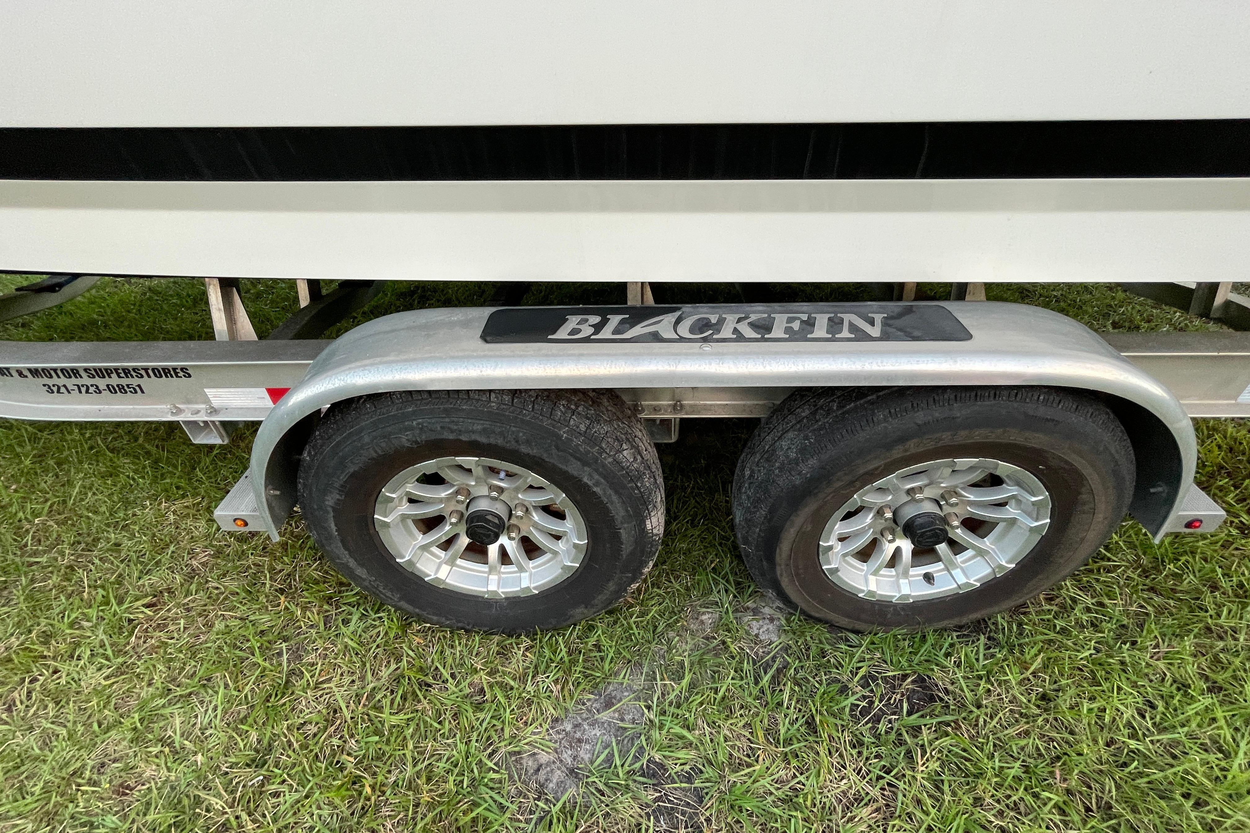 Trailer for 2022 Blackfin 252 CC boat on grass, featuring dual wheels.