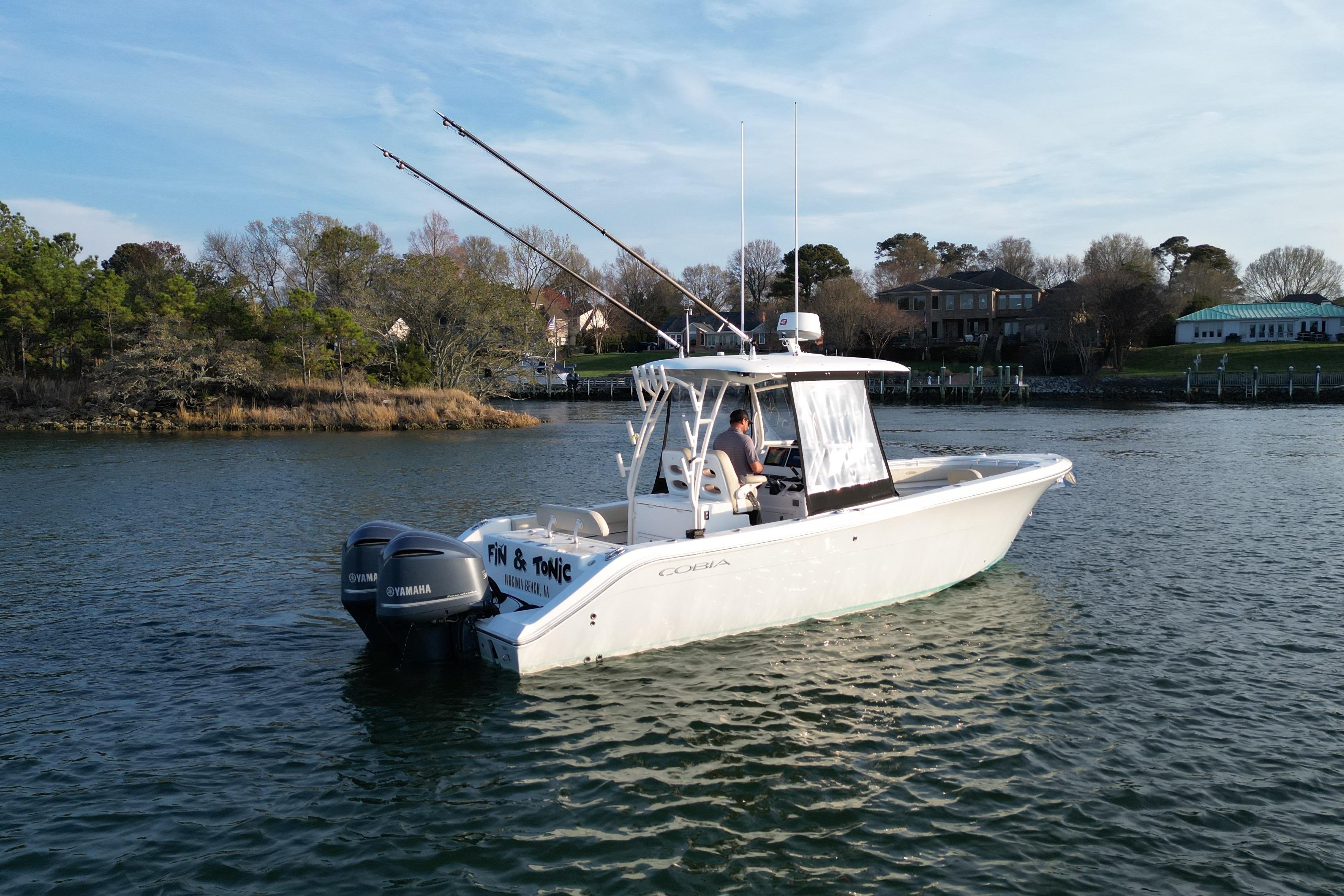 2016 Cobia 296 Center Console boat on calm water with fishing rods.
