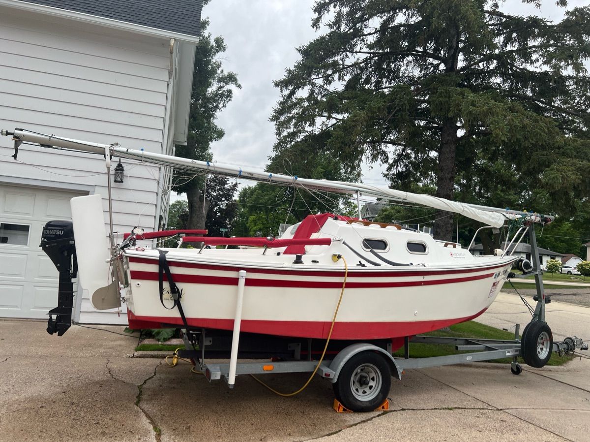 A white and red sailboat on a trailer in front of a house.