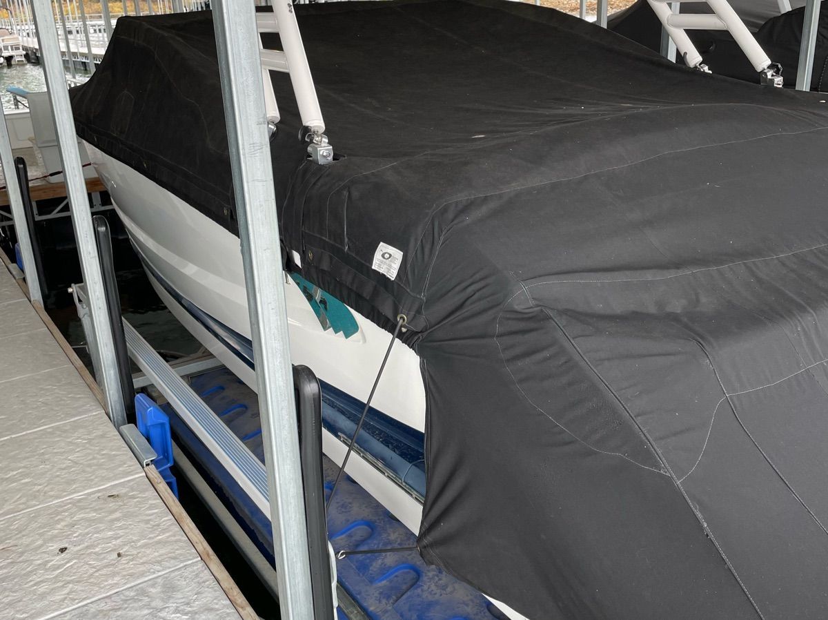 A 2011 Cobalt A25 boat is covered with a black tarp, docked in a marina.