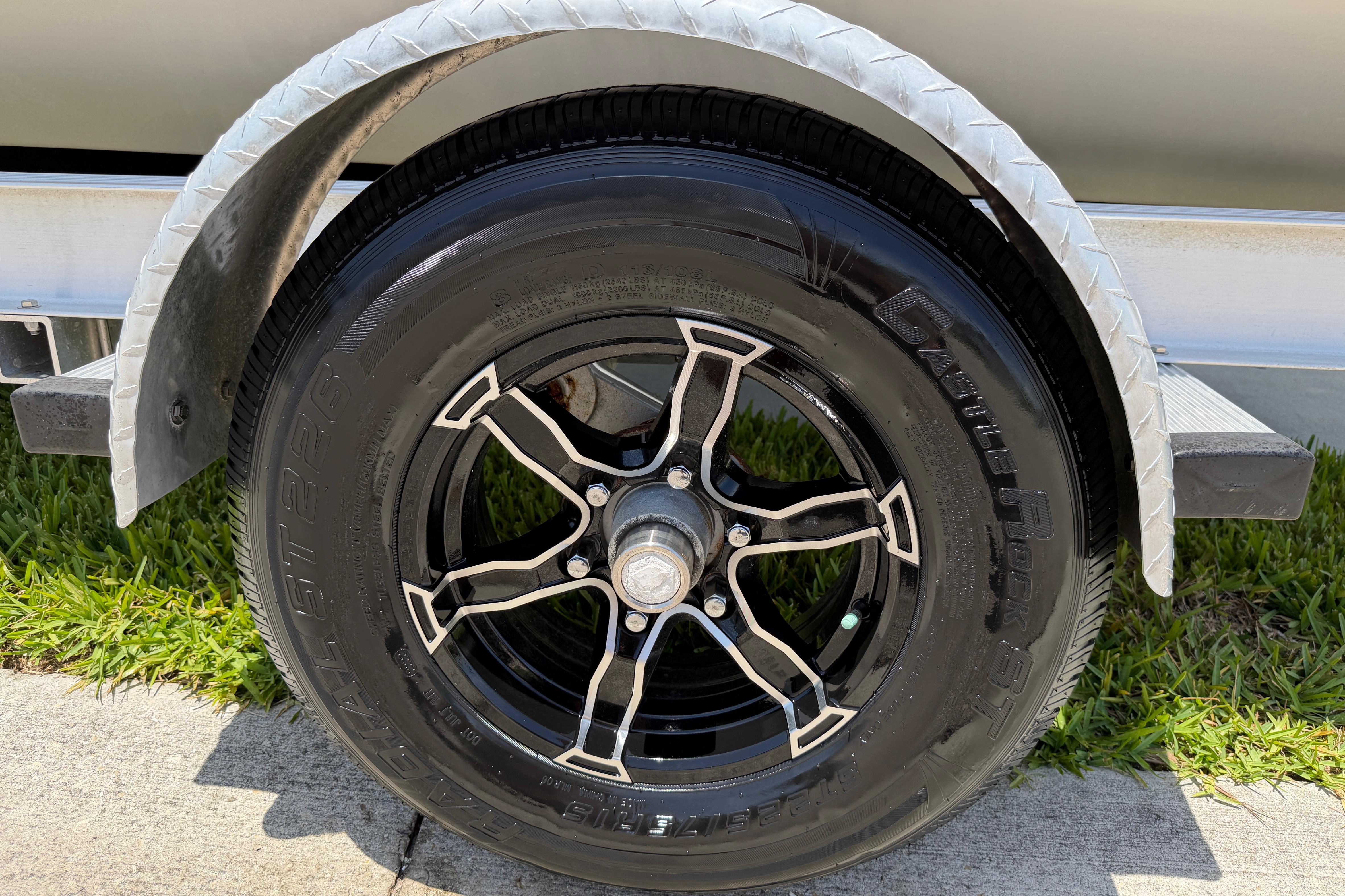 Trailer wheel of 2023 Carolina Skiff 21 LS boat on grass and pavement.