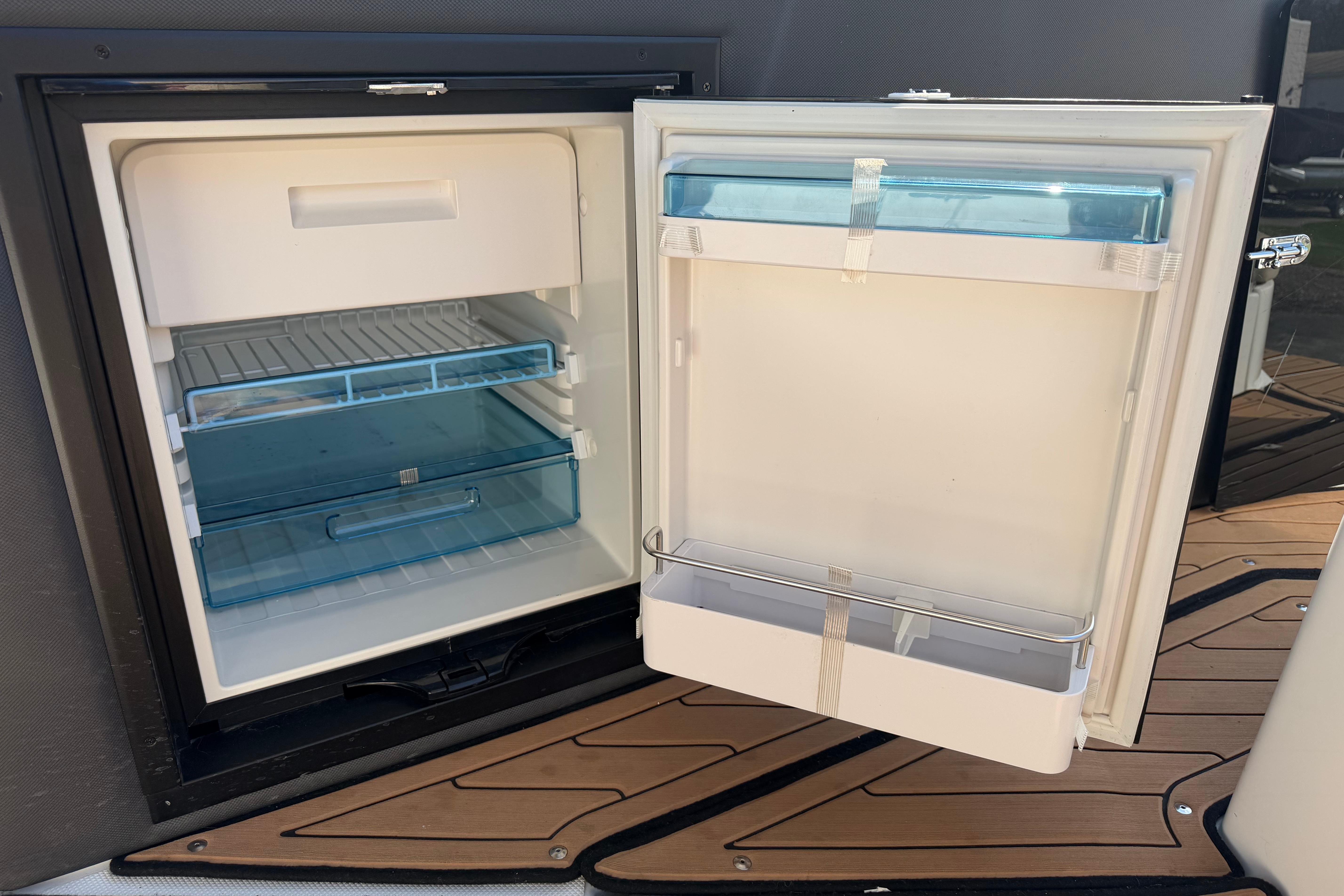 Open refrigerator on 2019 Rinker EX 320 boat, showcasing interior storage compartments.