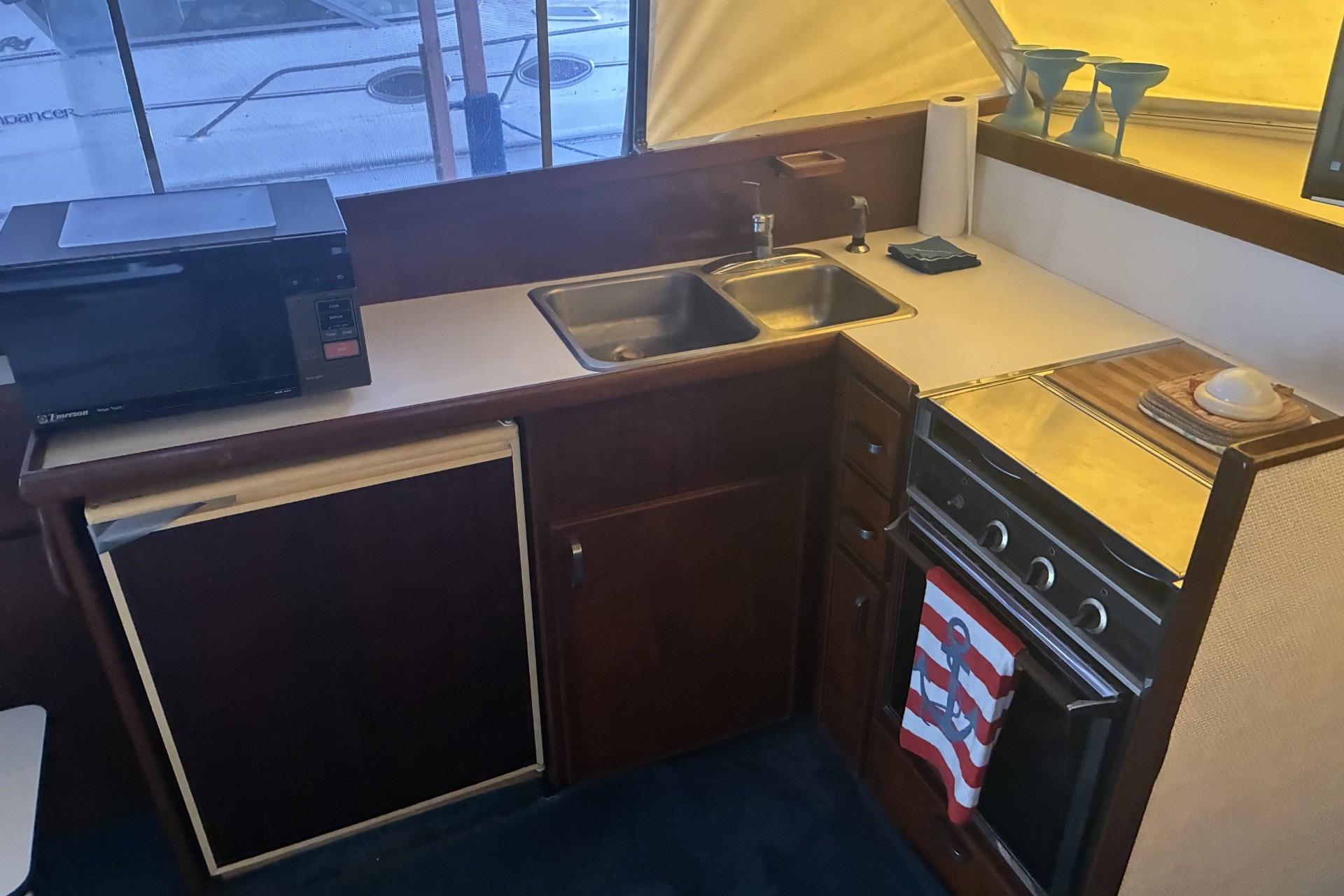 1980 Chris-Craft 360 Commander kitchen with stove, sink, microwave, and compact fridge.
