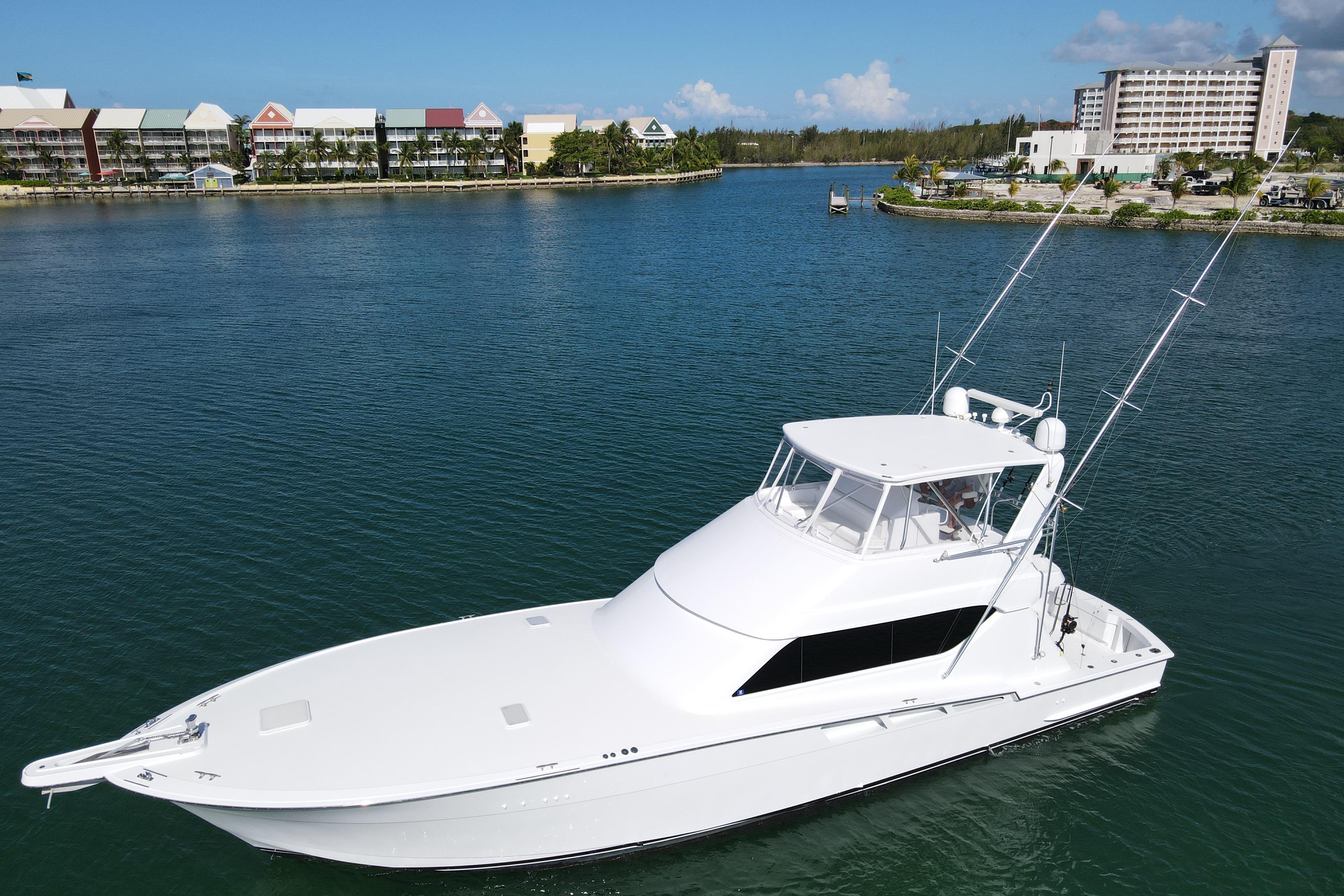2004 Hatteras 60 Convertible yacht on calm water, with scenic waterfront background.