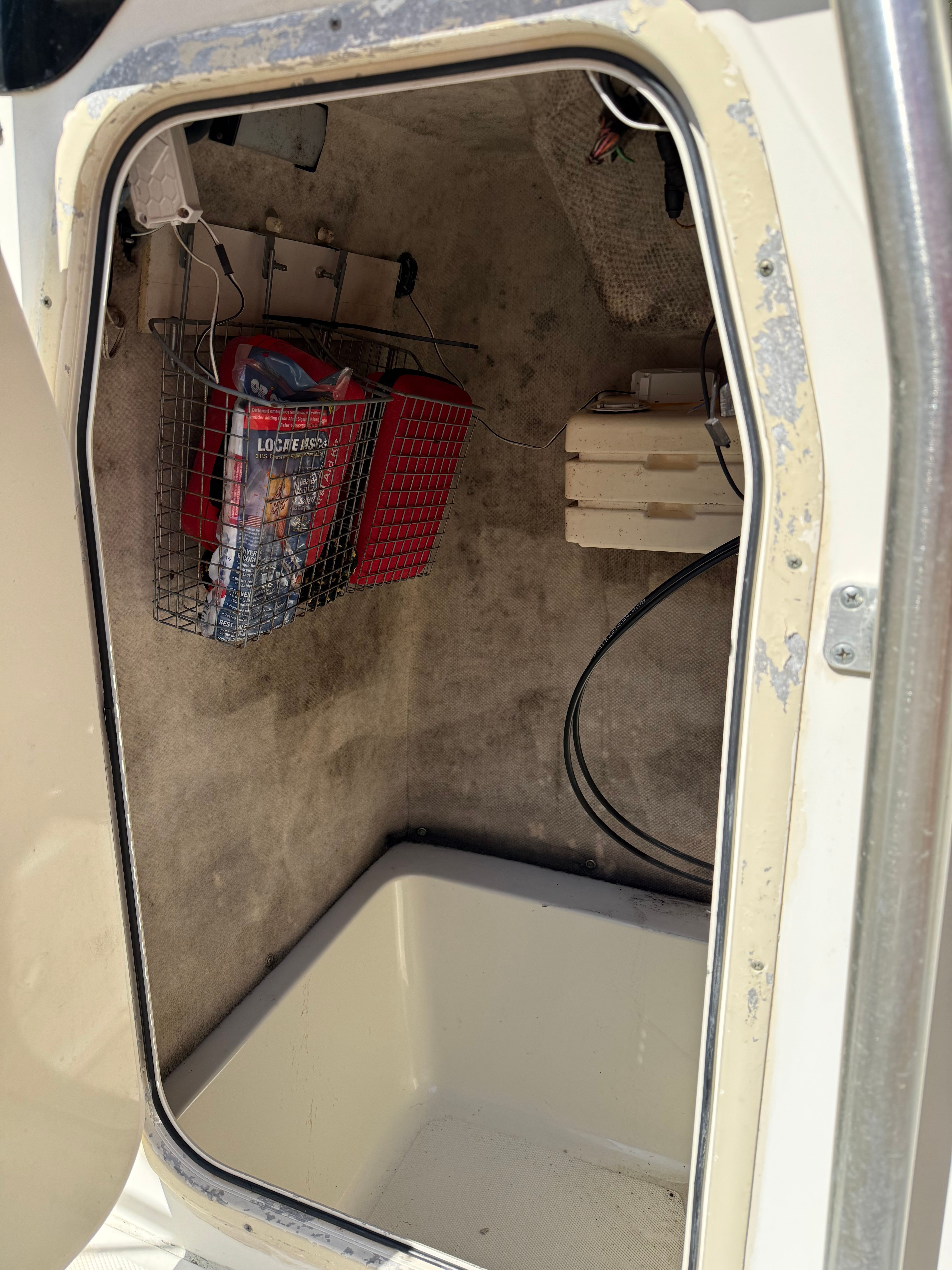 An open storage compartment with a wire basket and cables inside a boat.