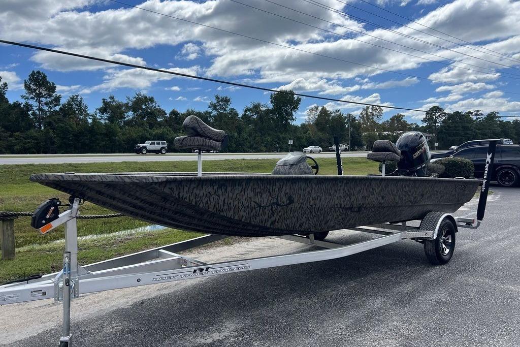 2026 Xpress XP200 boat on trailer, camo design, parked outdoors under cloudy sky.