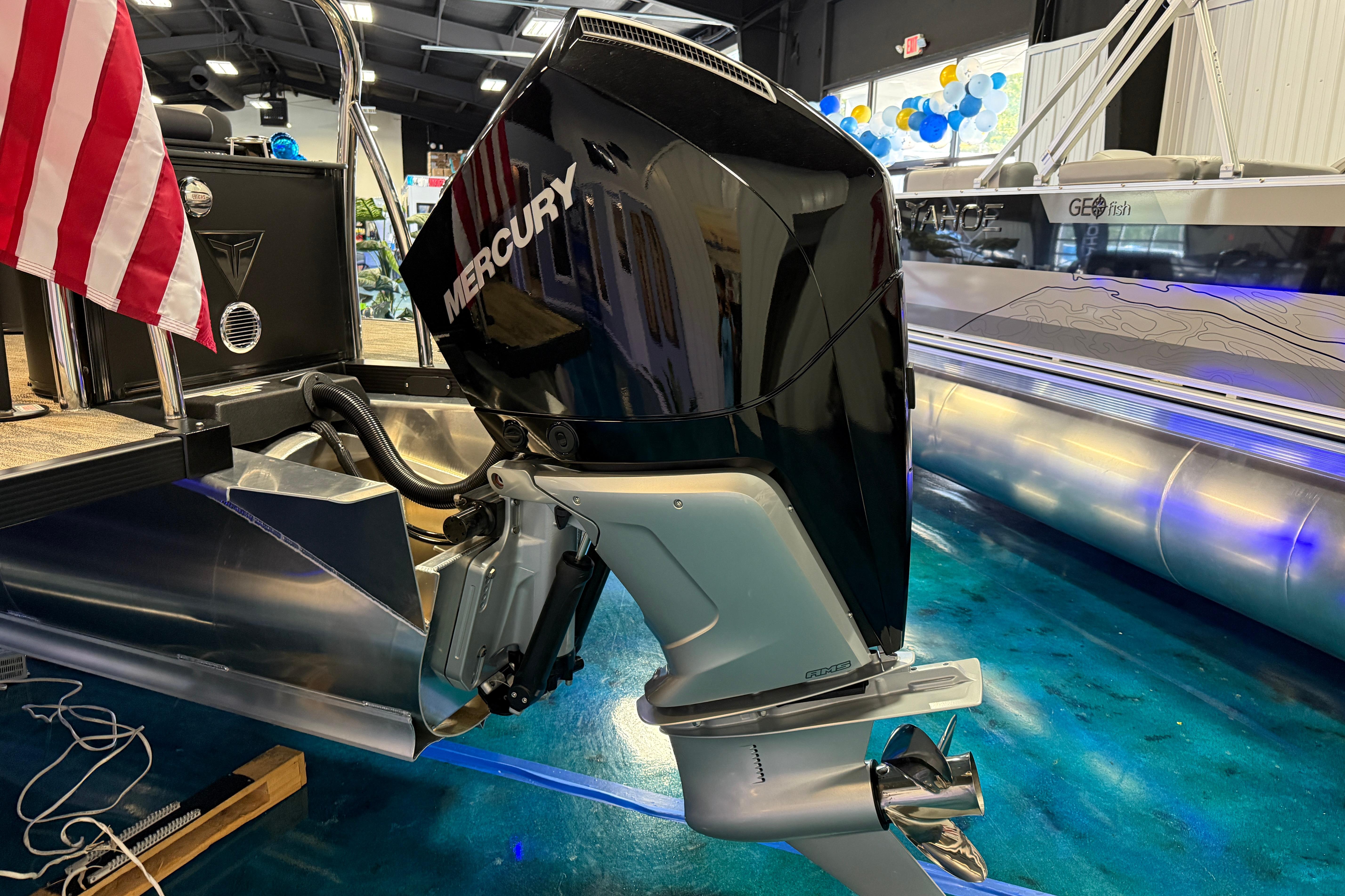 2026 Tahoe Pontoon Cascade Cruise with Mercury engine, displayed indoors with American flag.