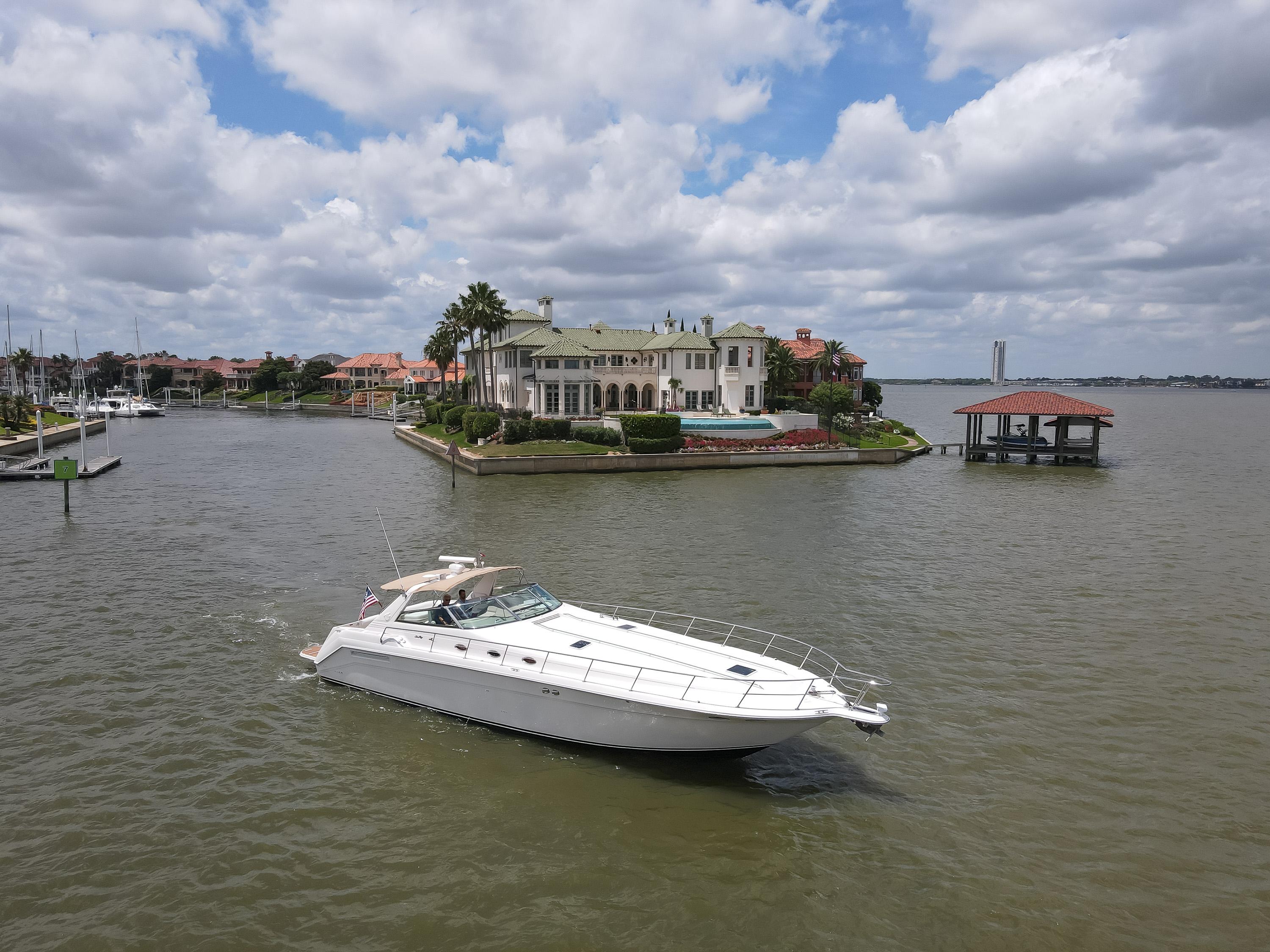 1996 Sea Ray 500 Sundancer yacht cruising near luxurious waterfront mansion.