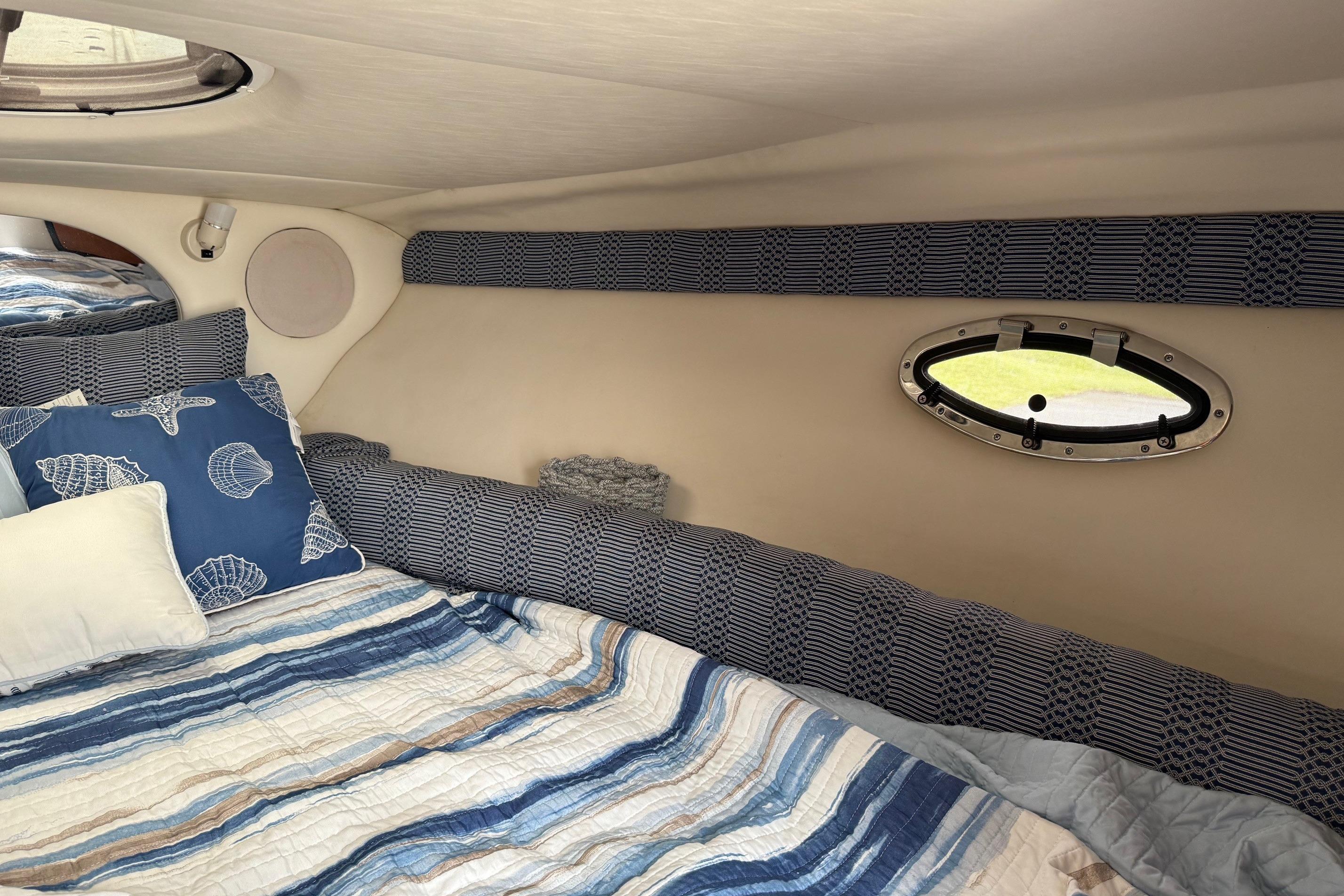 Cozy cabin interior of 2005 Crownline 250 CR boat with nautical-themed bedding.