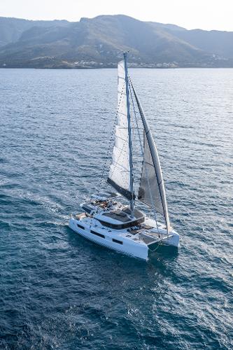 2025 Lagoon 51 ICONIC catamaran sailing on open sea with mountainous backdrop.
