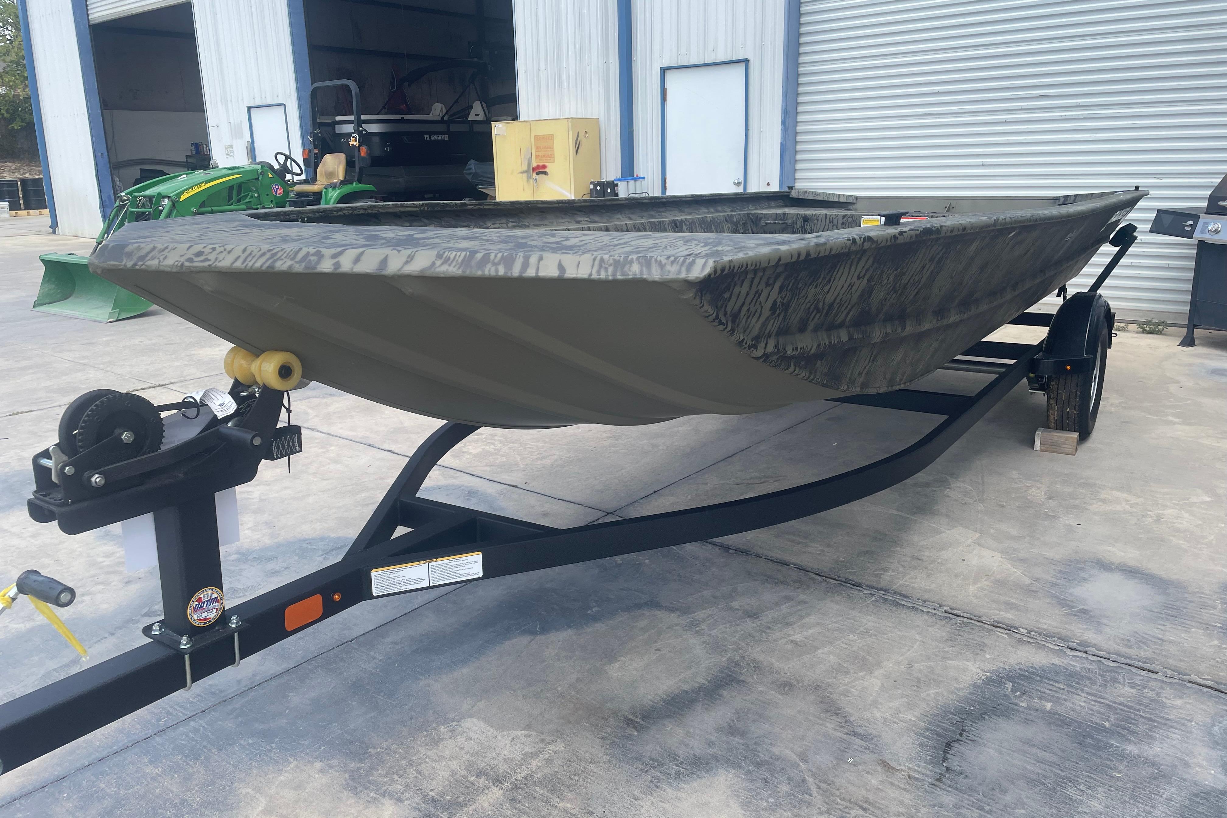 2026 Tracker Grizzly 1860 Utility boat on trailer, parked outside a warehouse.