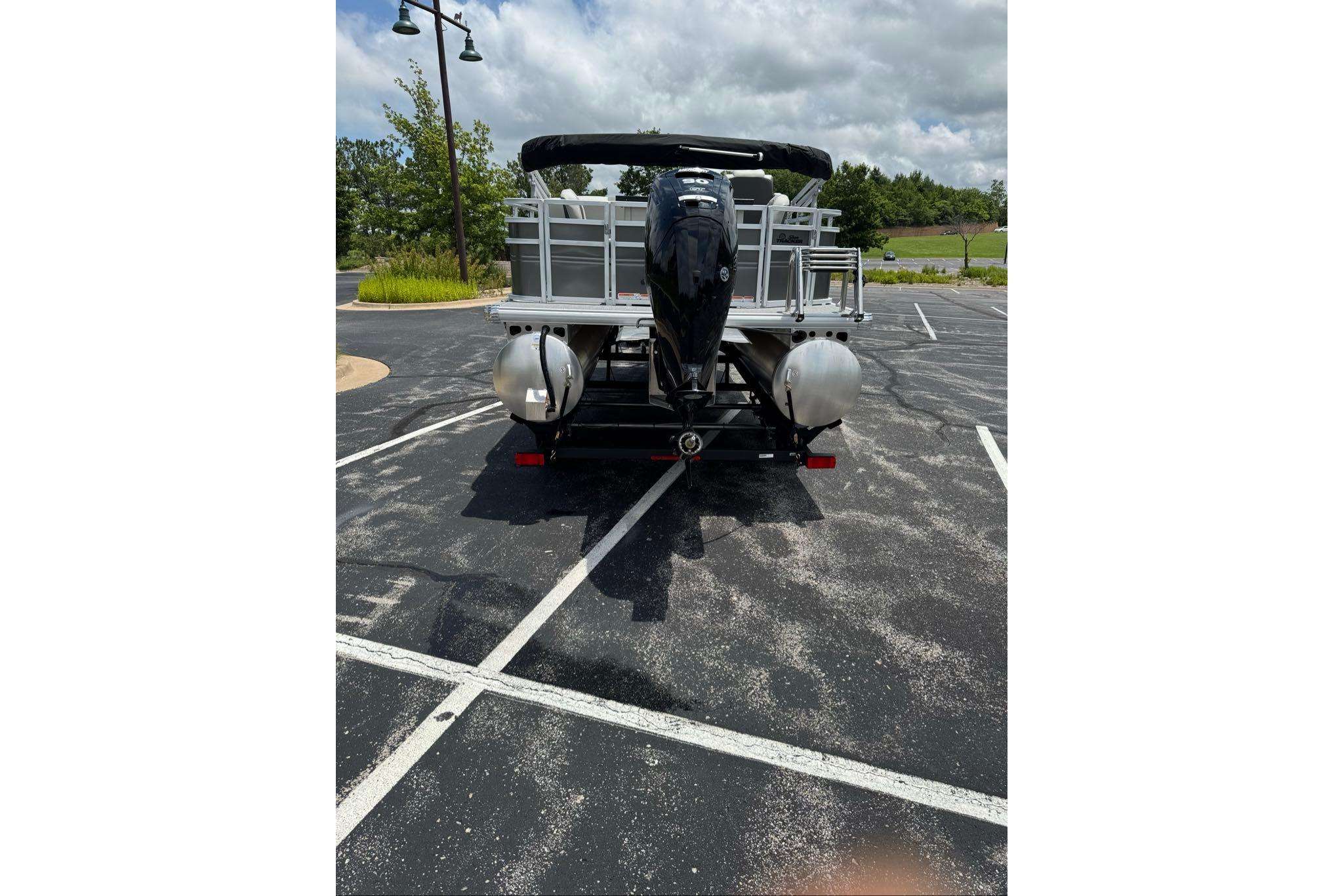 2026 Sun Tracker Fishin' Barge 20 DLX pontoon boat in parking lot, rear view.