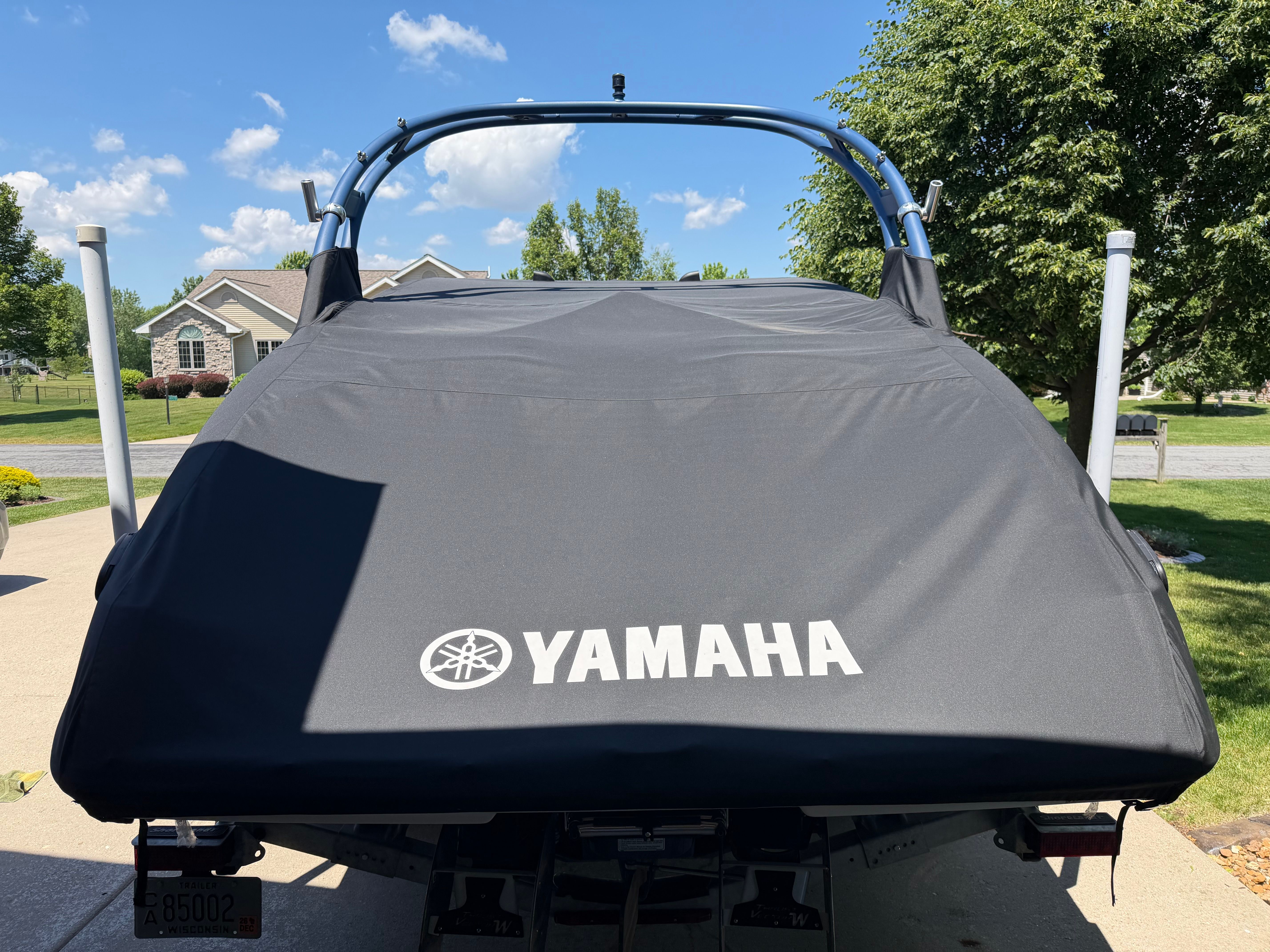 A Yamaha boat with a cover is on a trailer in a residential area.