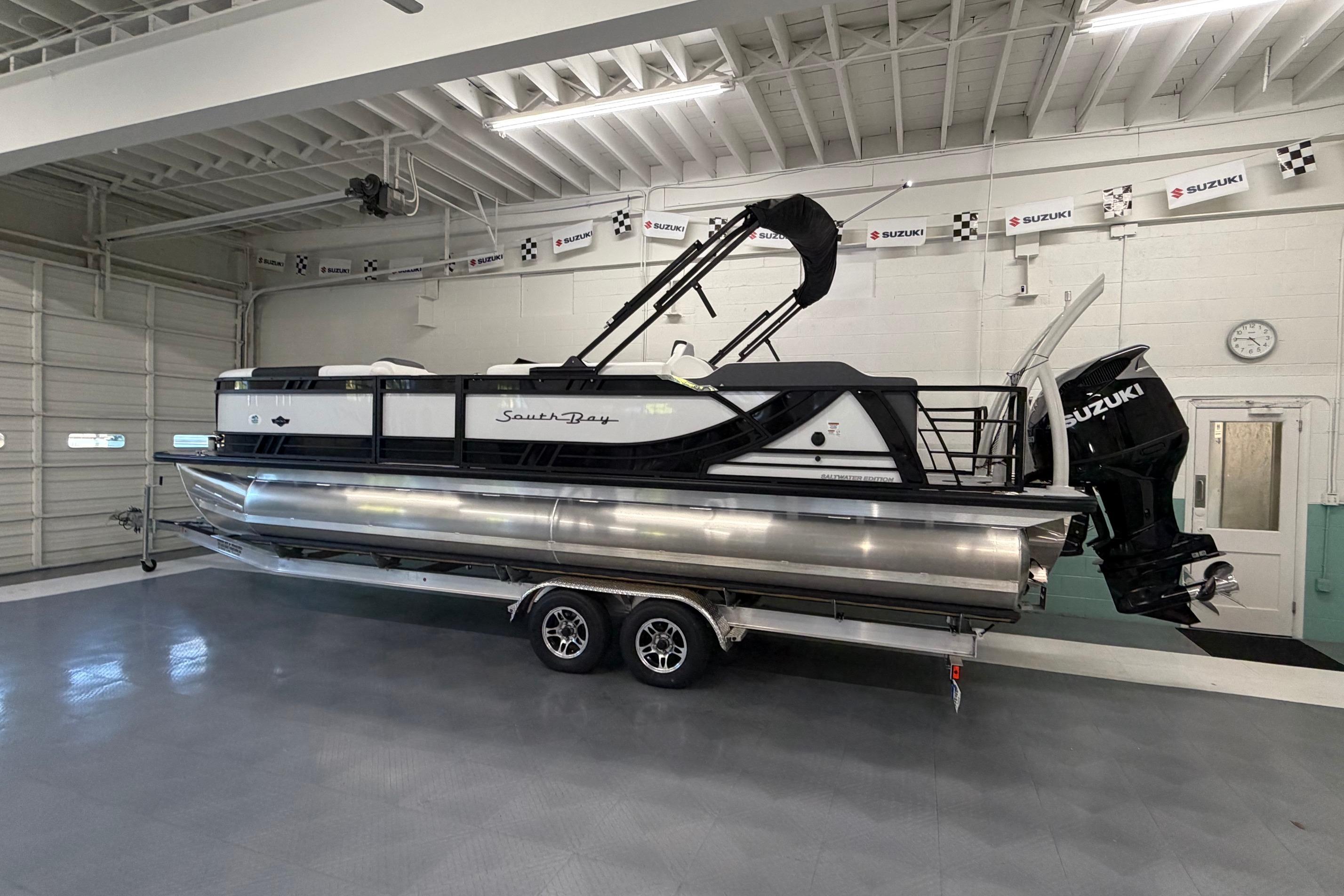 2026 South Bay 525SB2 pontoon boat with Suzuki engine in a showroom.