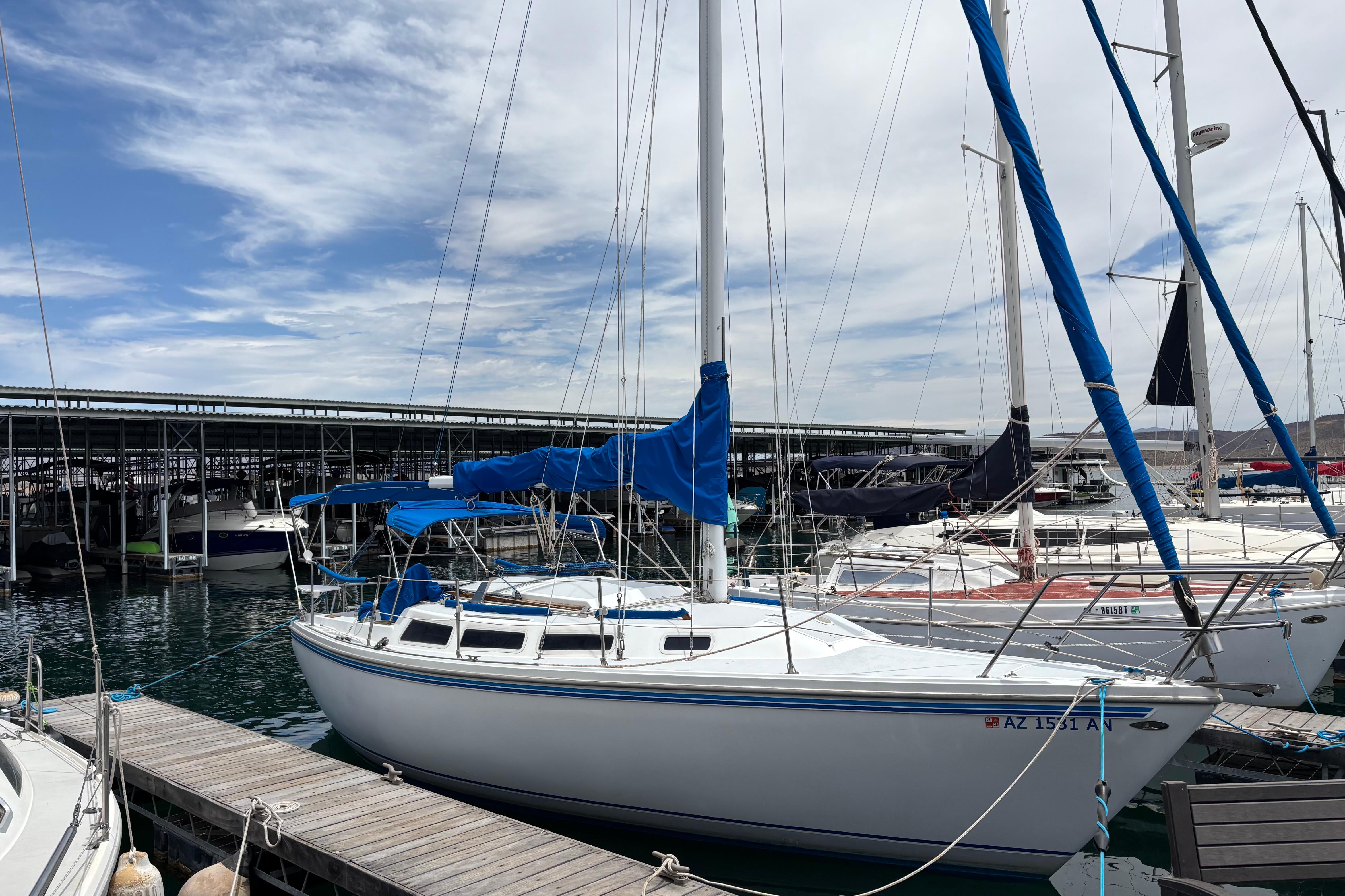 1980 Catalina 30 sailboat docked at marina under a partly cloudy sky.