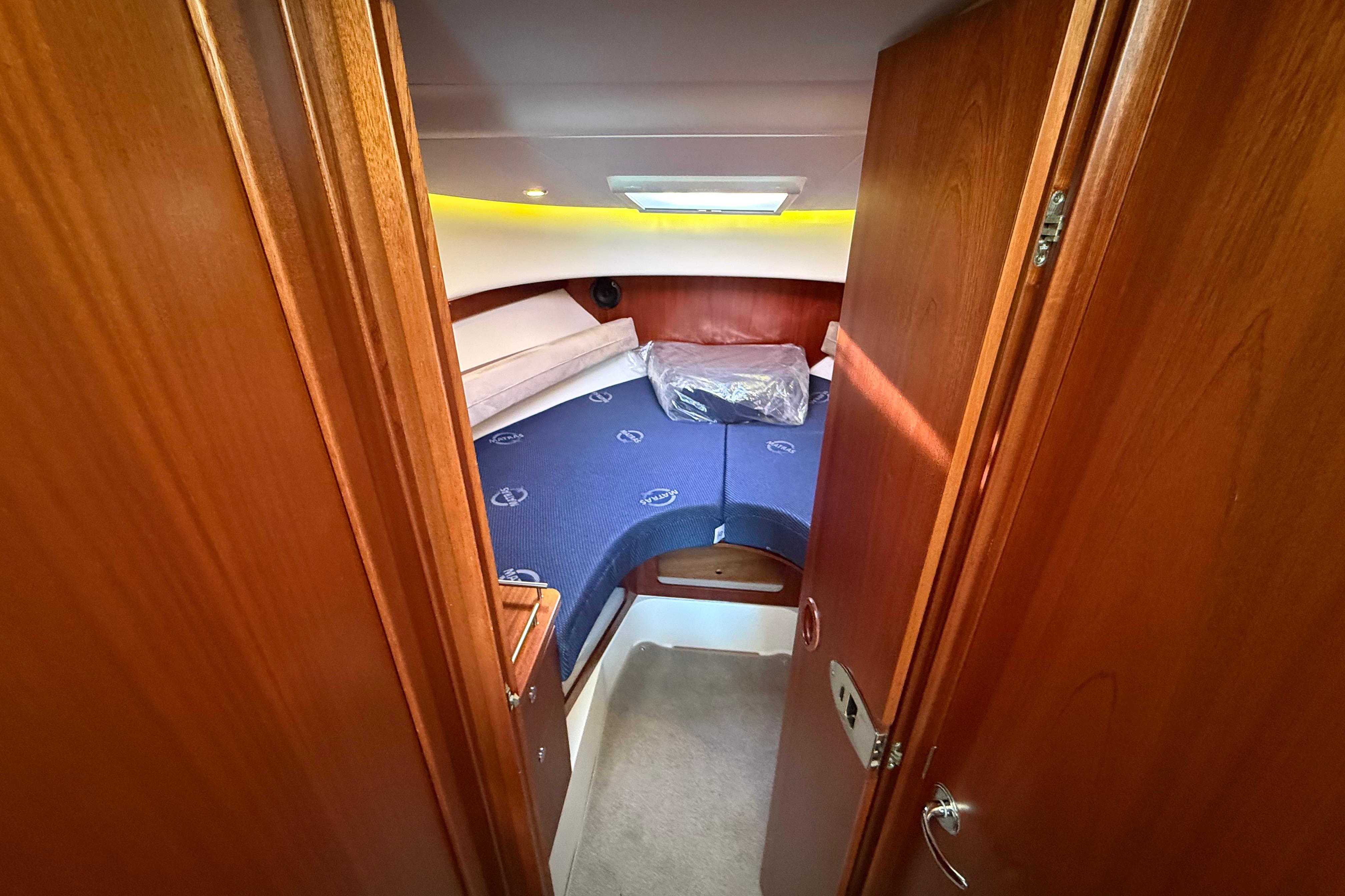 Cozy cabin interior of 2011 Nimbus 335 Coupe with wooden finish and blue bedding.