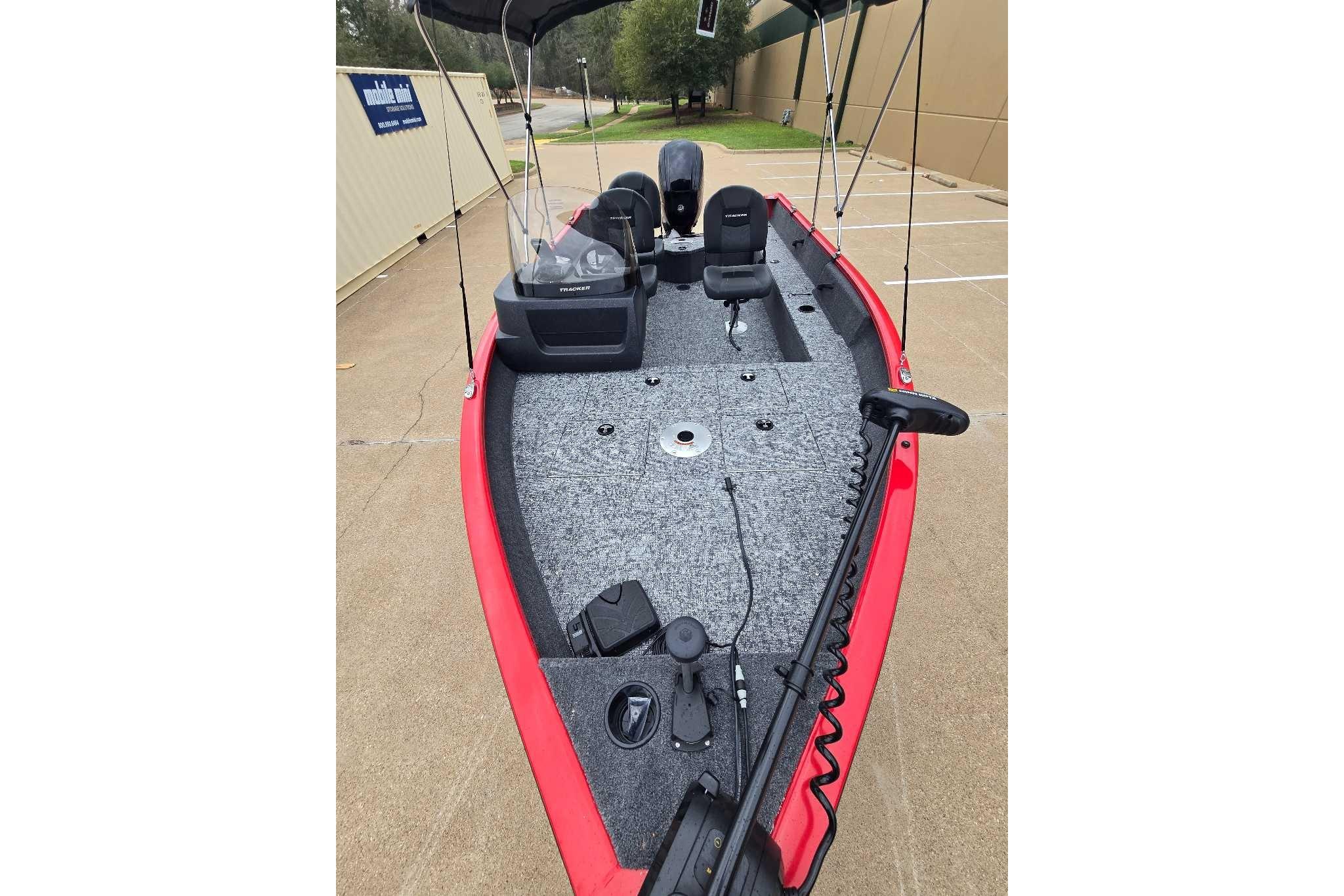 2026 Tracker Pro Guide V-16 SC boat with red exterior and gray interior, parked outdoors.