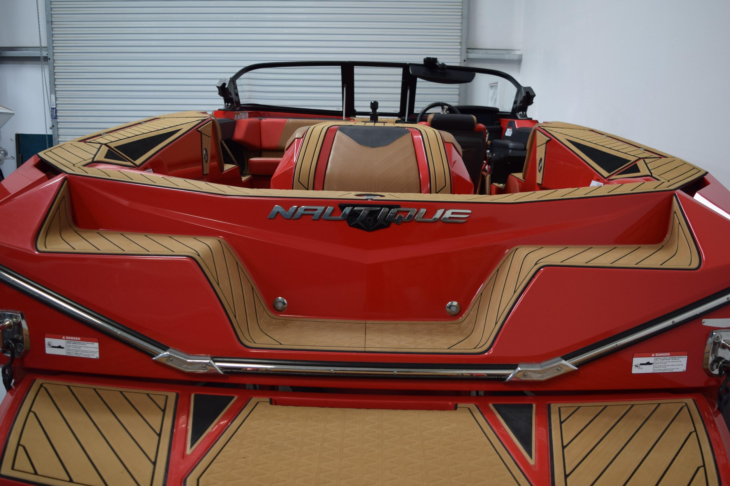 2024 Nautique Ski Nautique boat, red and tan interior, rear view in a garage.