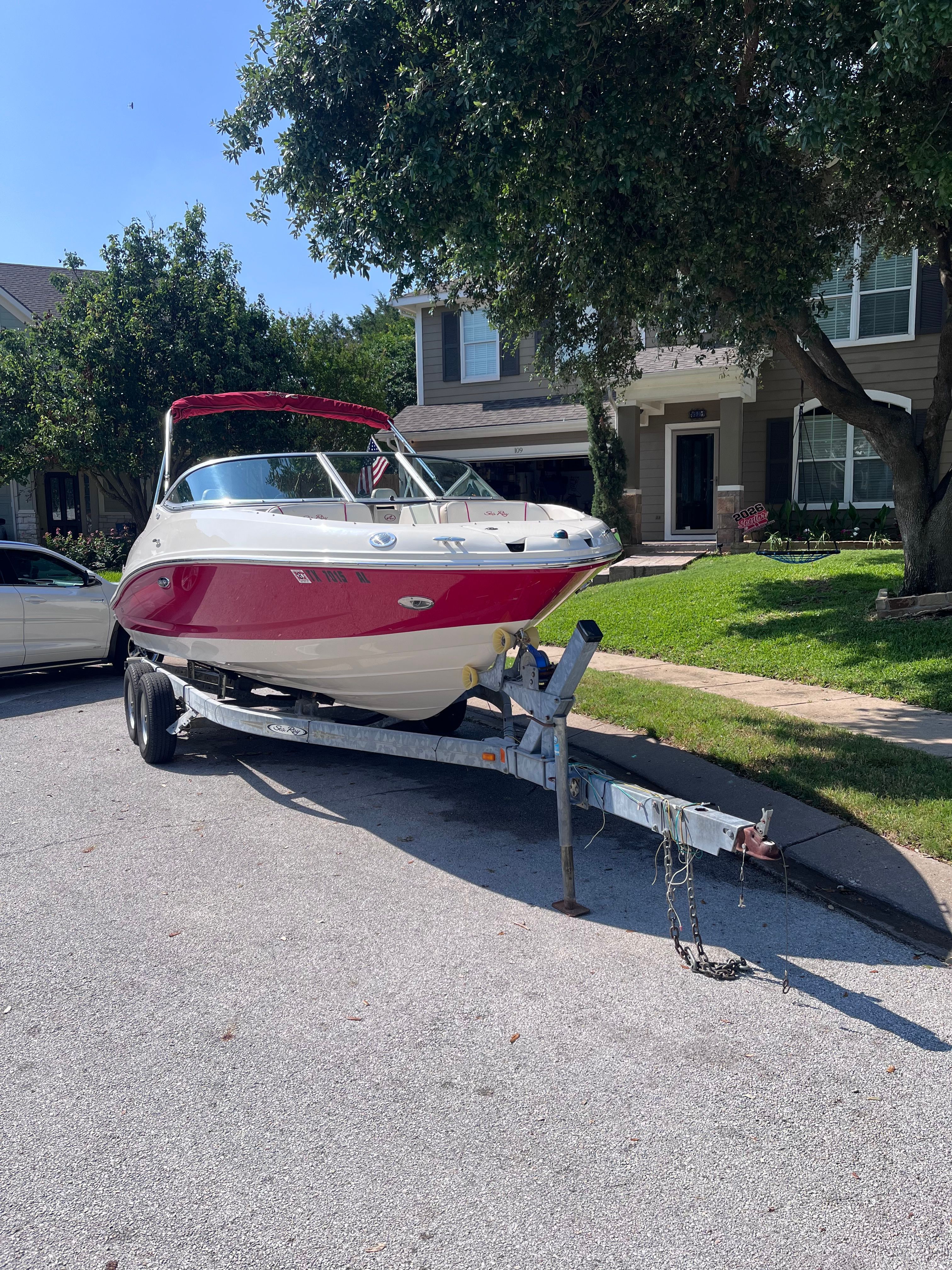 A red 2007 Sea Ray 210 Select boat on a trailer in a residential street.
