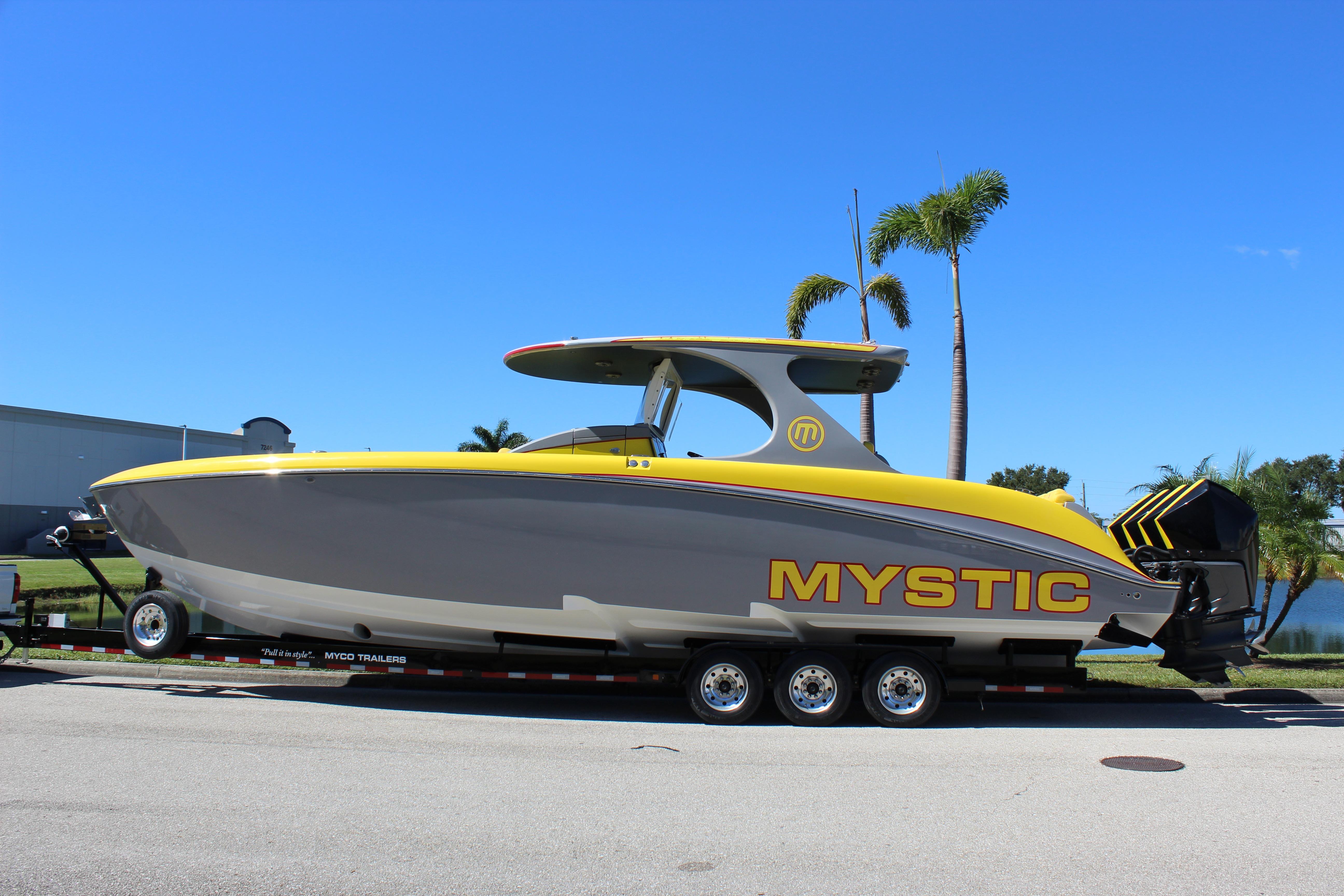 2021 Mystic M4200 boat on trailer, yellow and gray design, palm trees in background.