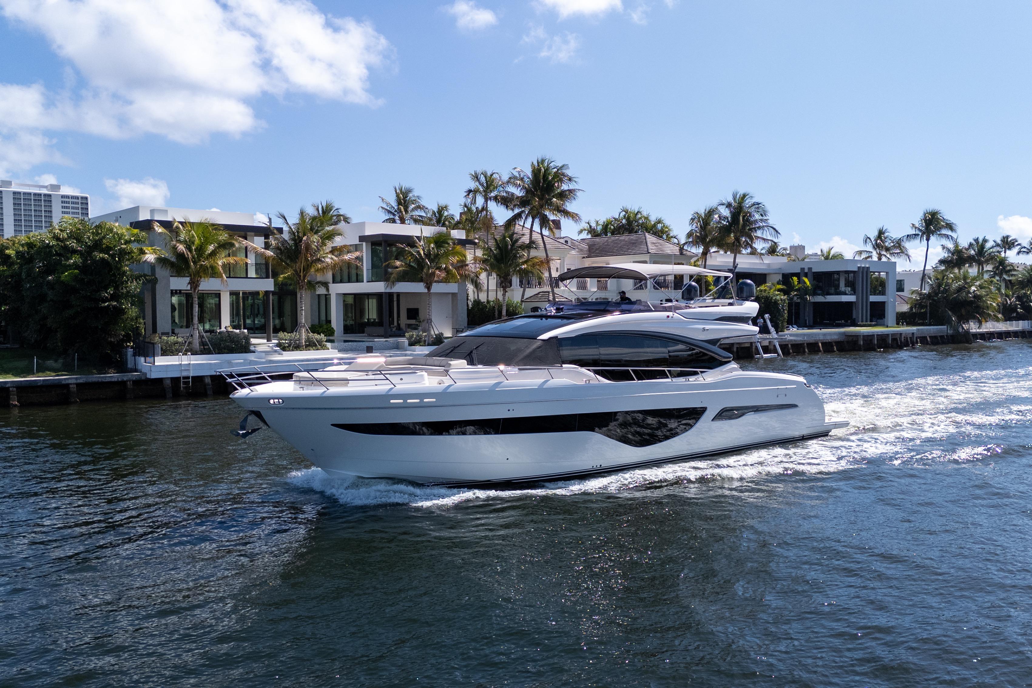 Luxurious 2019 Princess S78 yacht cruising near waterfront homes under a clear blue sky.