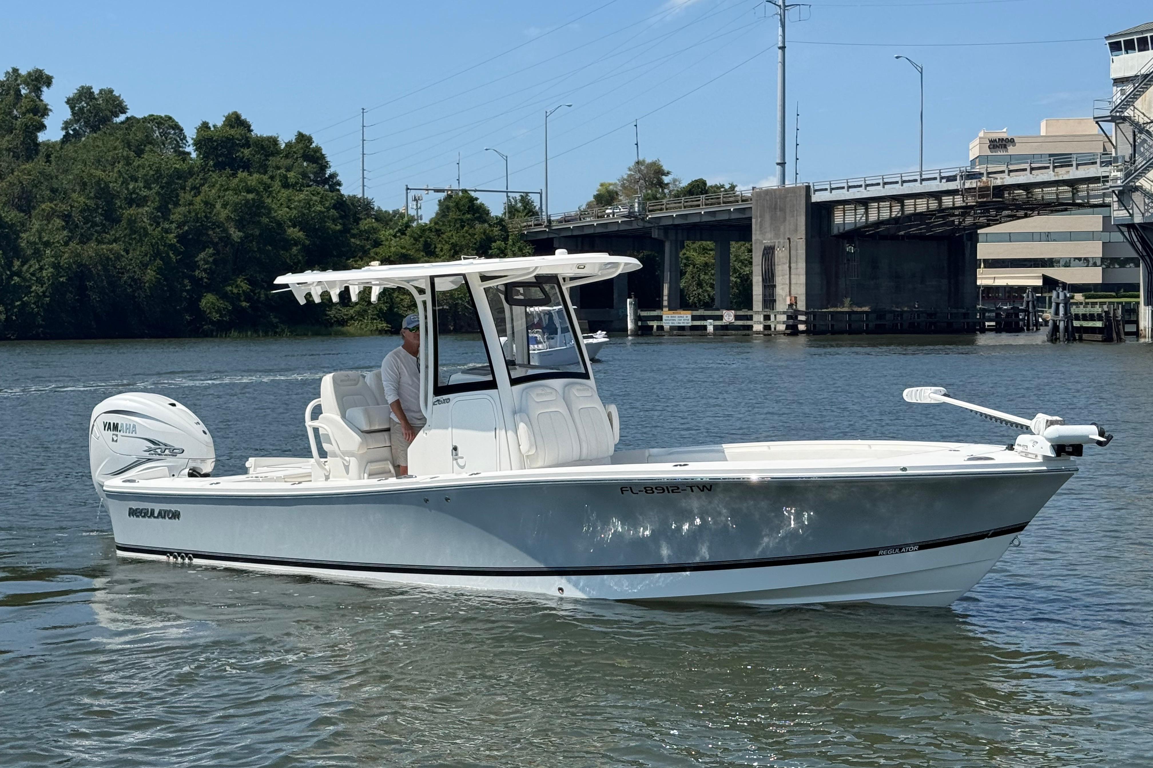 2023 Regulator 26XO boat cruising on a river near a bridge.
