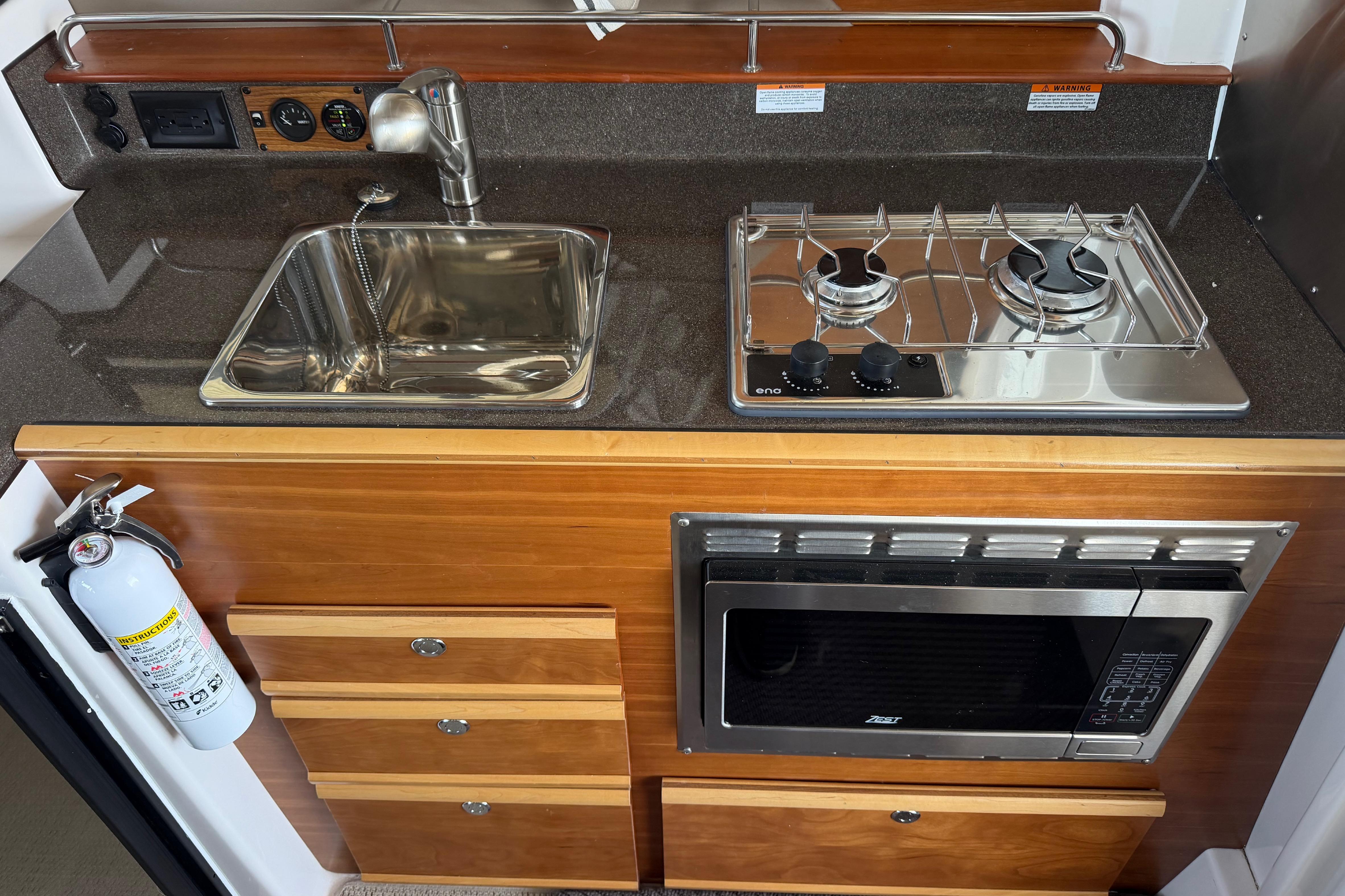 2023 Cutwater C-288 Coupe kitchen with sink, stove, microwave, and fire extinguisher.