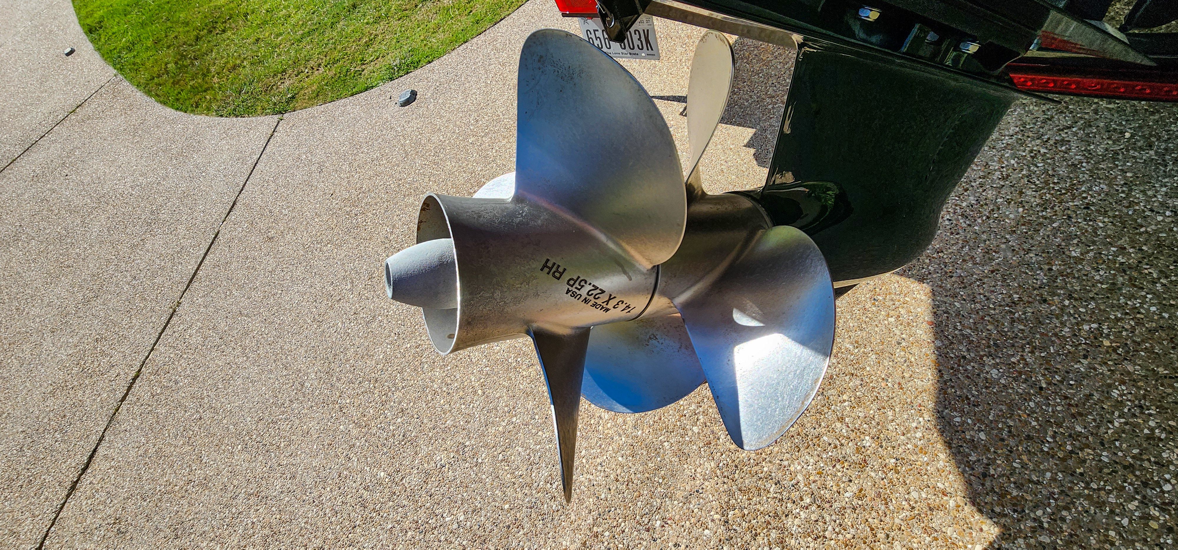 Close-up of a shiny propeller on a boat, situated on a paved area.