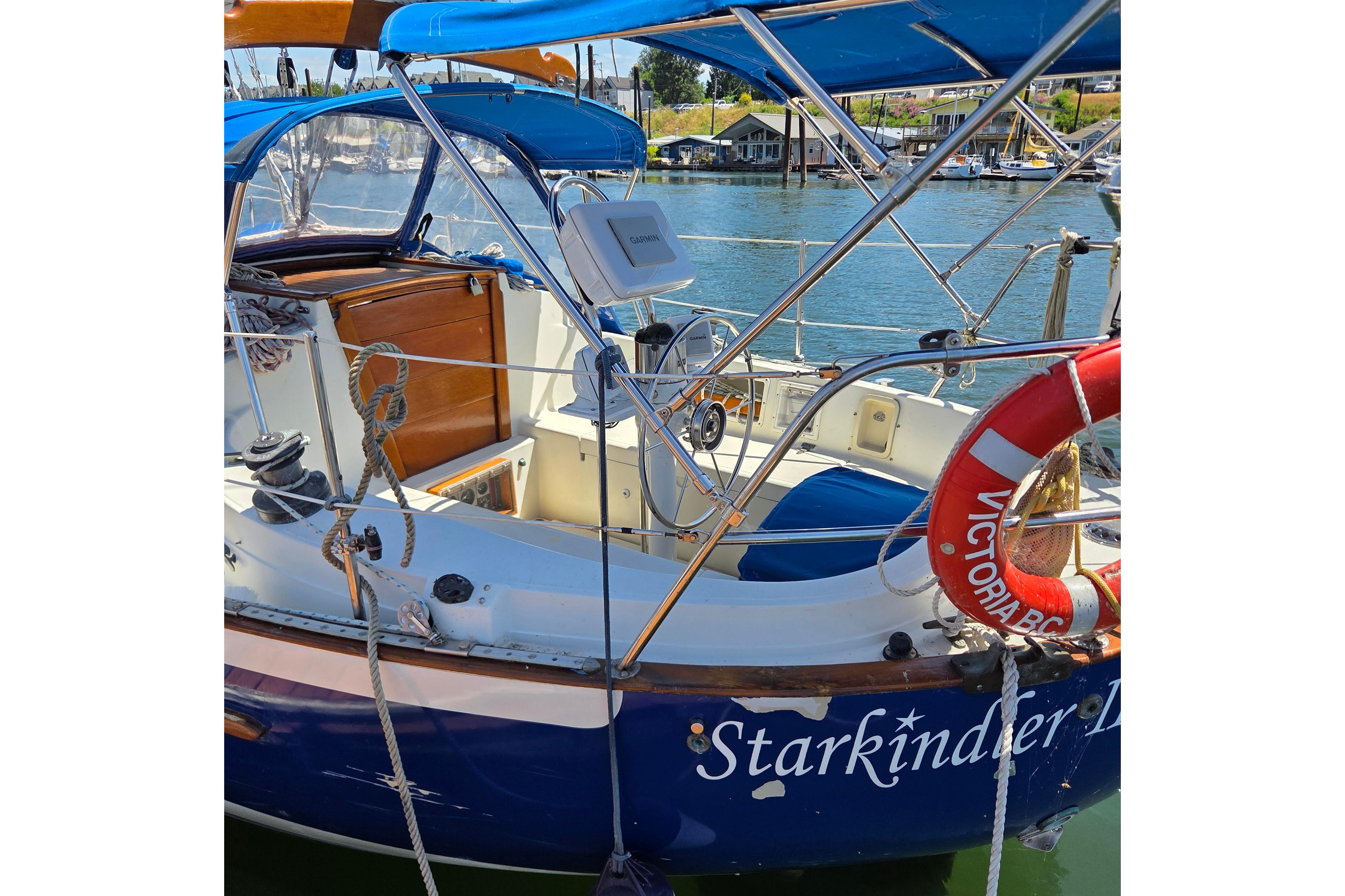1983 Pacific Seacraft 34 sailboat docked, featuring a blue canopy and lifebuoy.