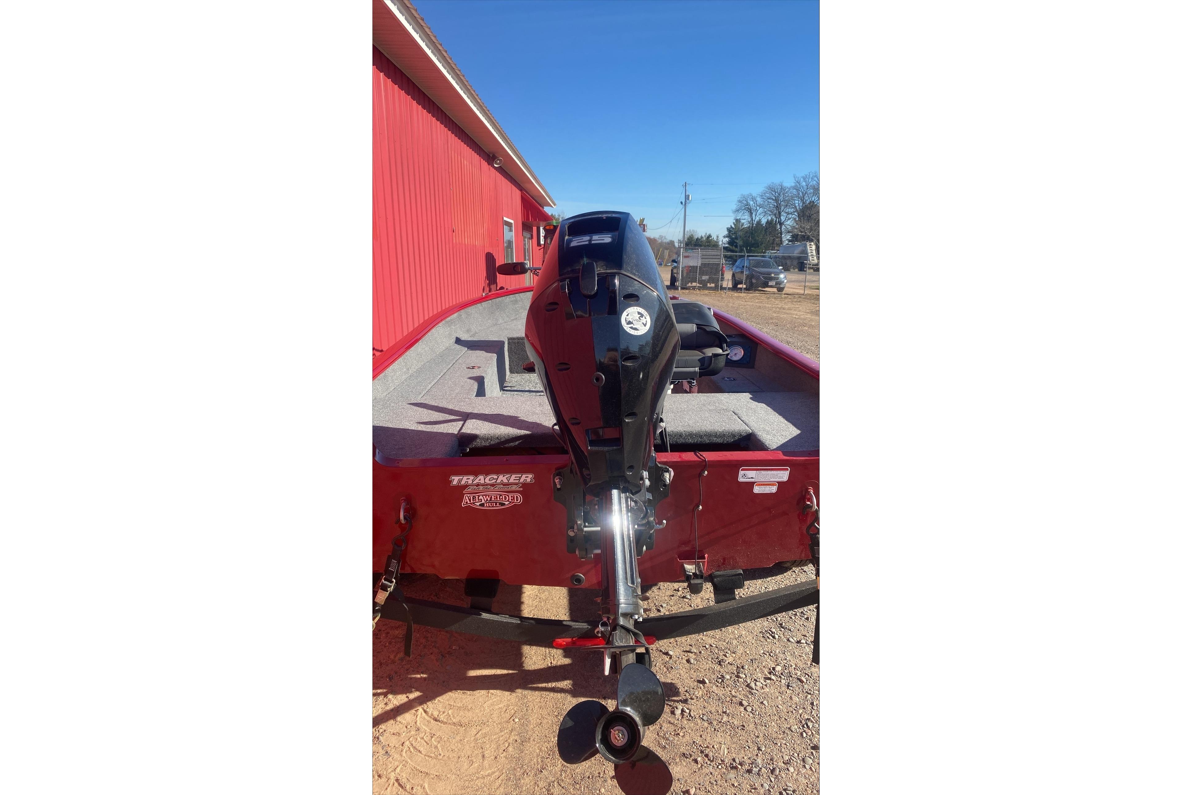 2025 Tracker Super Guide V-16 T boat with outboard motor, parked near a red building.