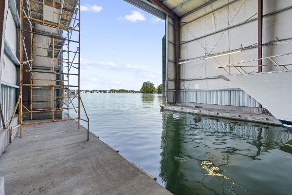 Boathouse interior with water view, scaffolding, and partial boat, Custom Larson Boathouse, 1985.