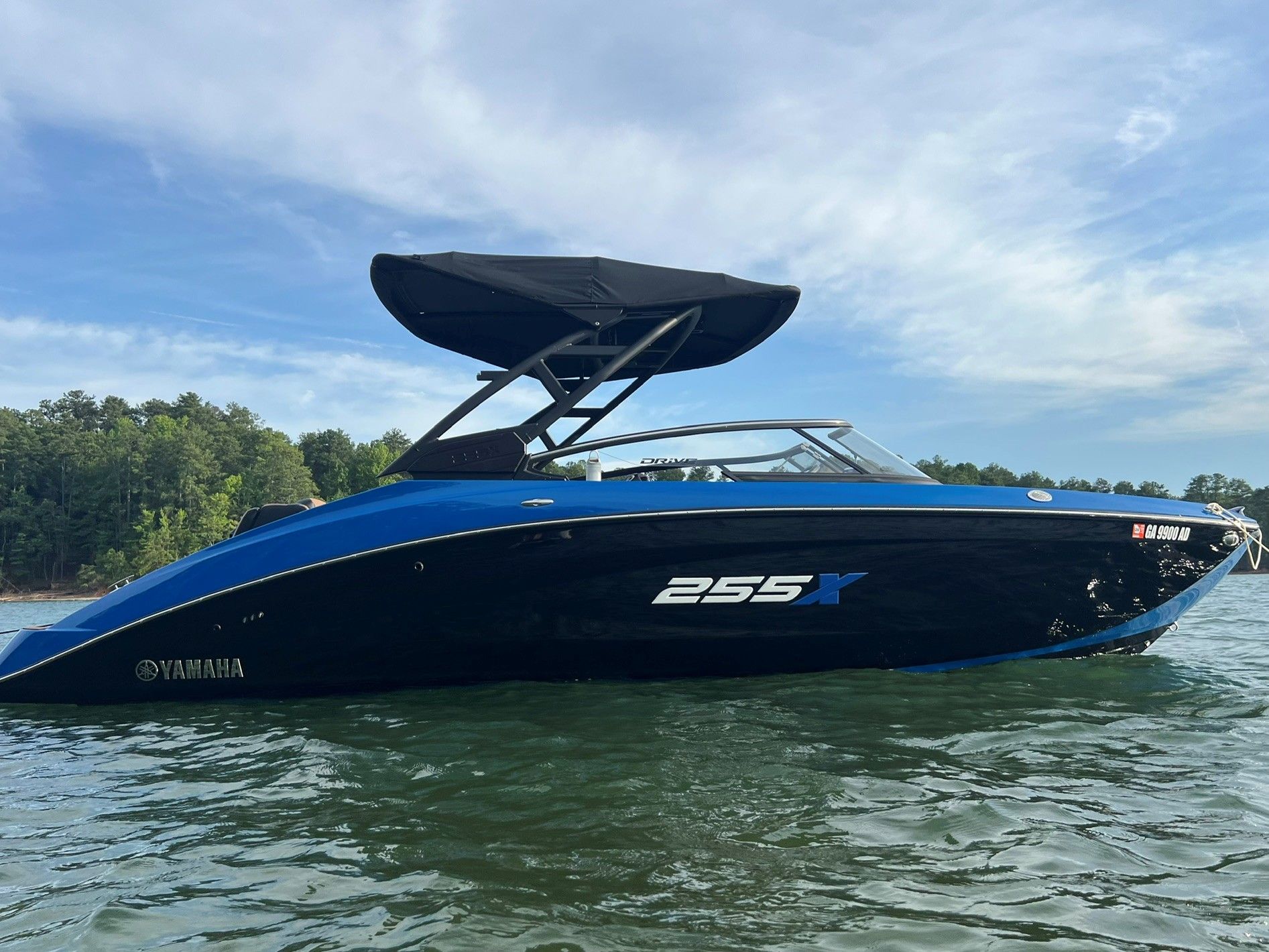 A blue Yamaha 255XD boat floats on a calm lake with a wooded shoreline in the background.