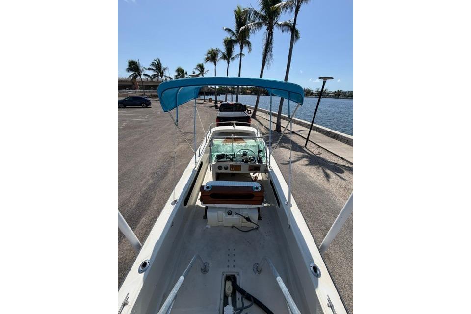 1990 Boston Whaler 17 Newport boat with blue canopy, parked near waterfront and palm trees.