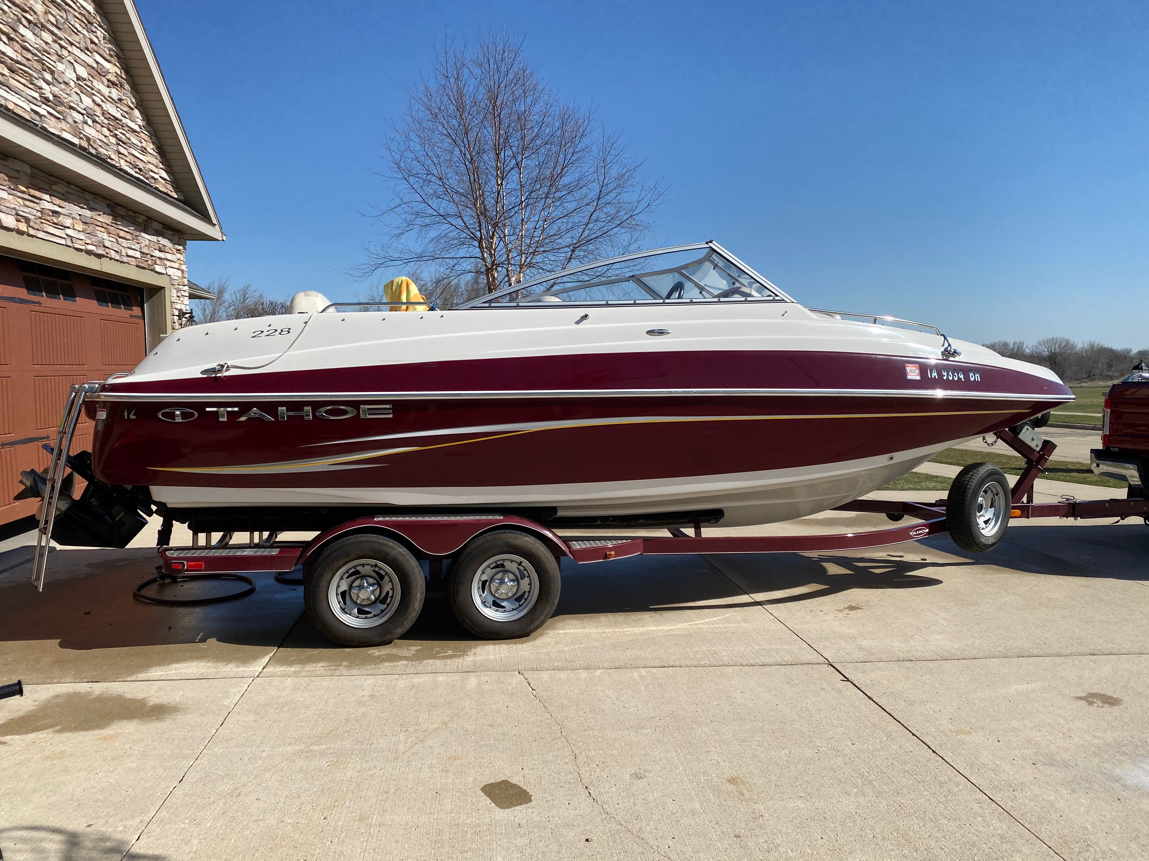 A 2011 Tahoe 228 boat on a trailer, parked on a driveway next to a house.