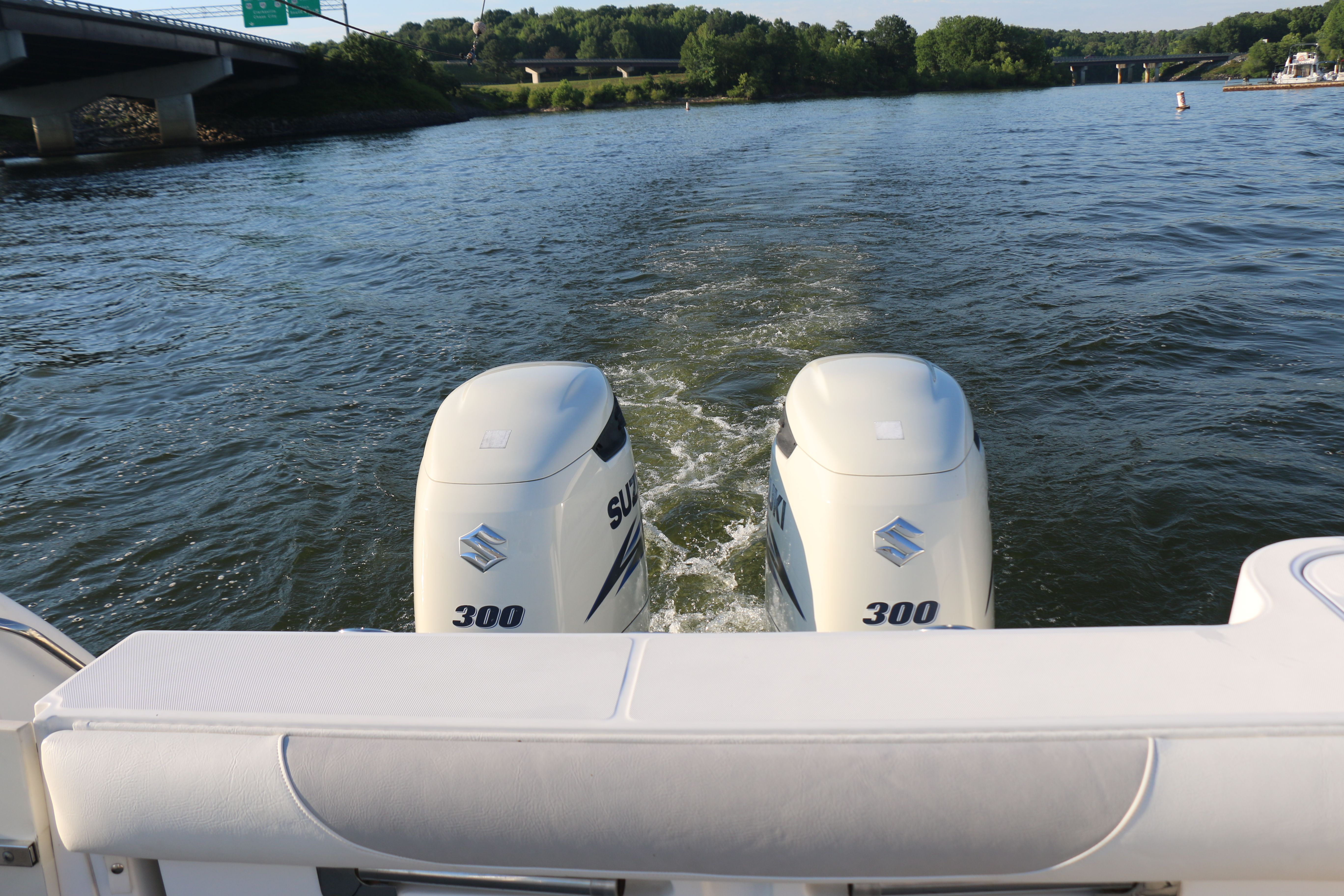 Two outboard motors on a boat in the water, surrounded by green landscape.