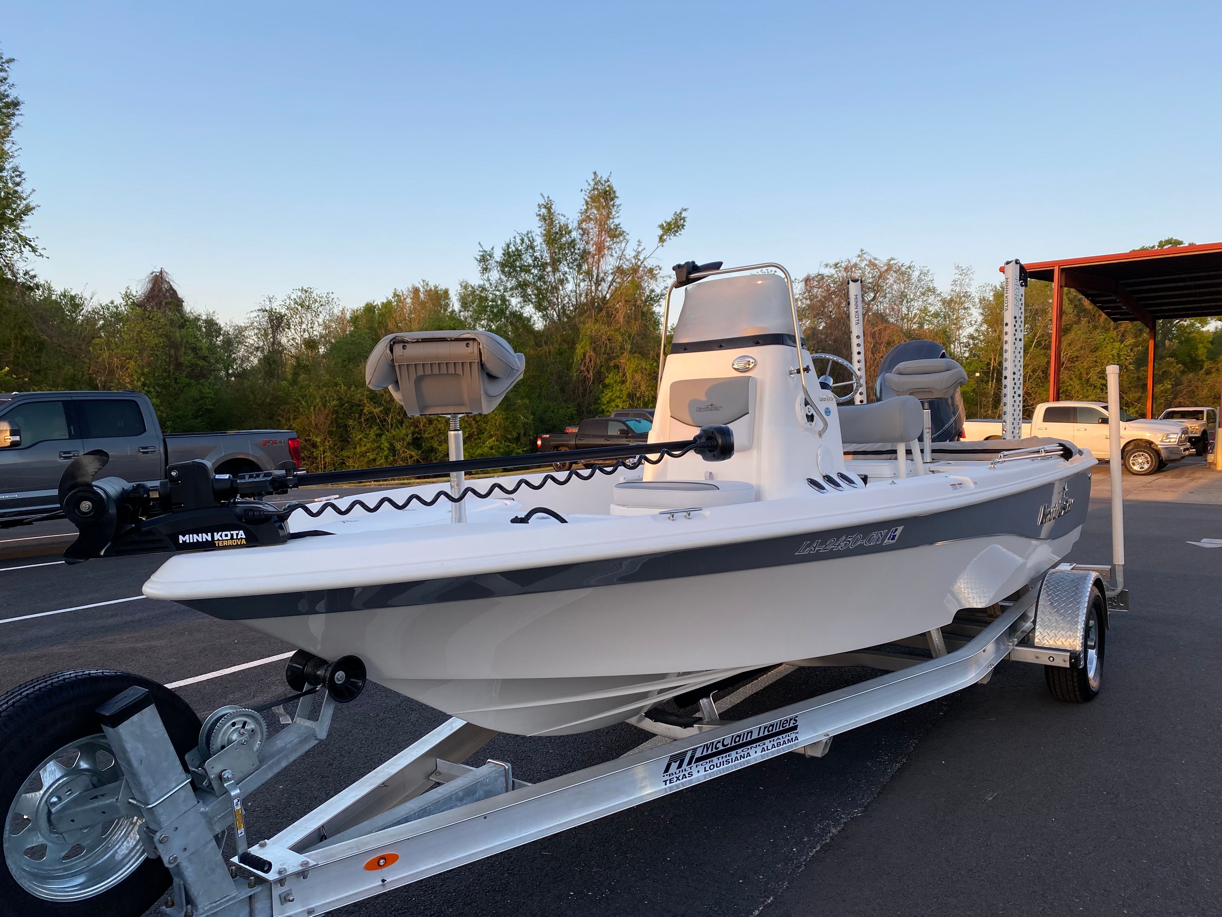 A white 2021 NauticStar 195 XTS boat on a trailer outdoors, with trees in the background.