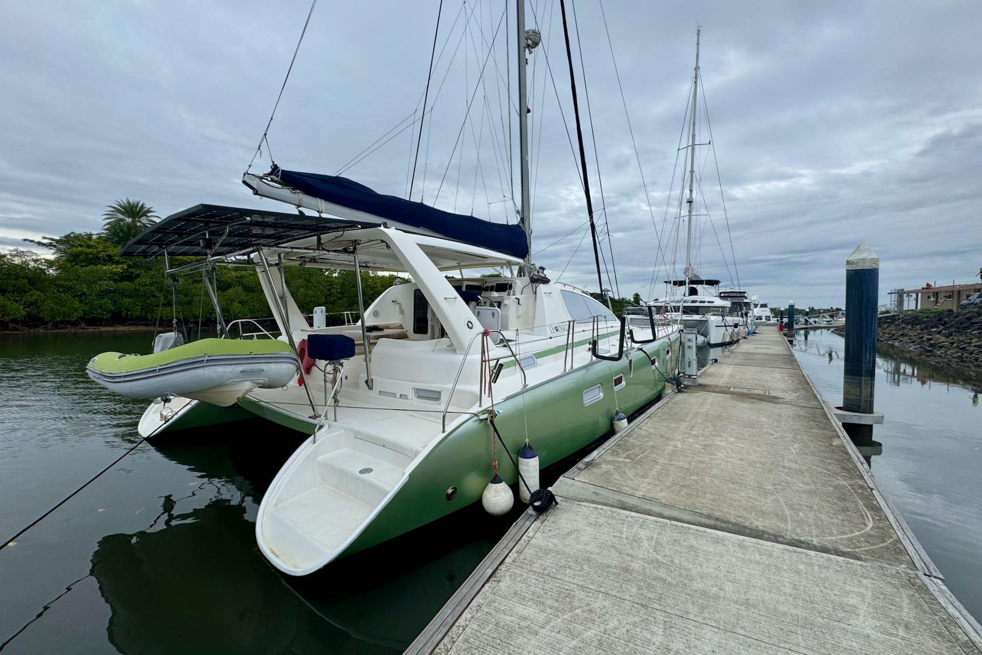 2004 Leopard 42 catamaran docked at marina, overcast sky, lush greenery in background.