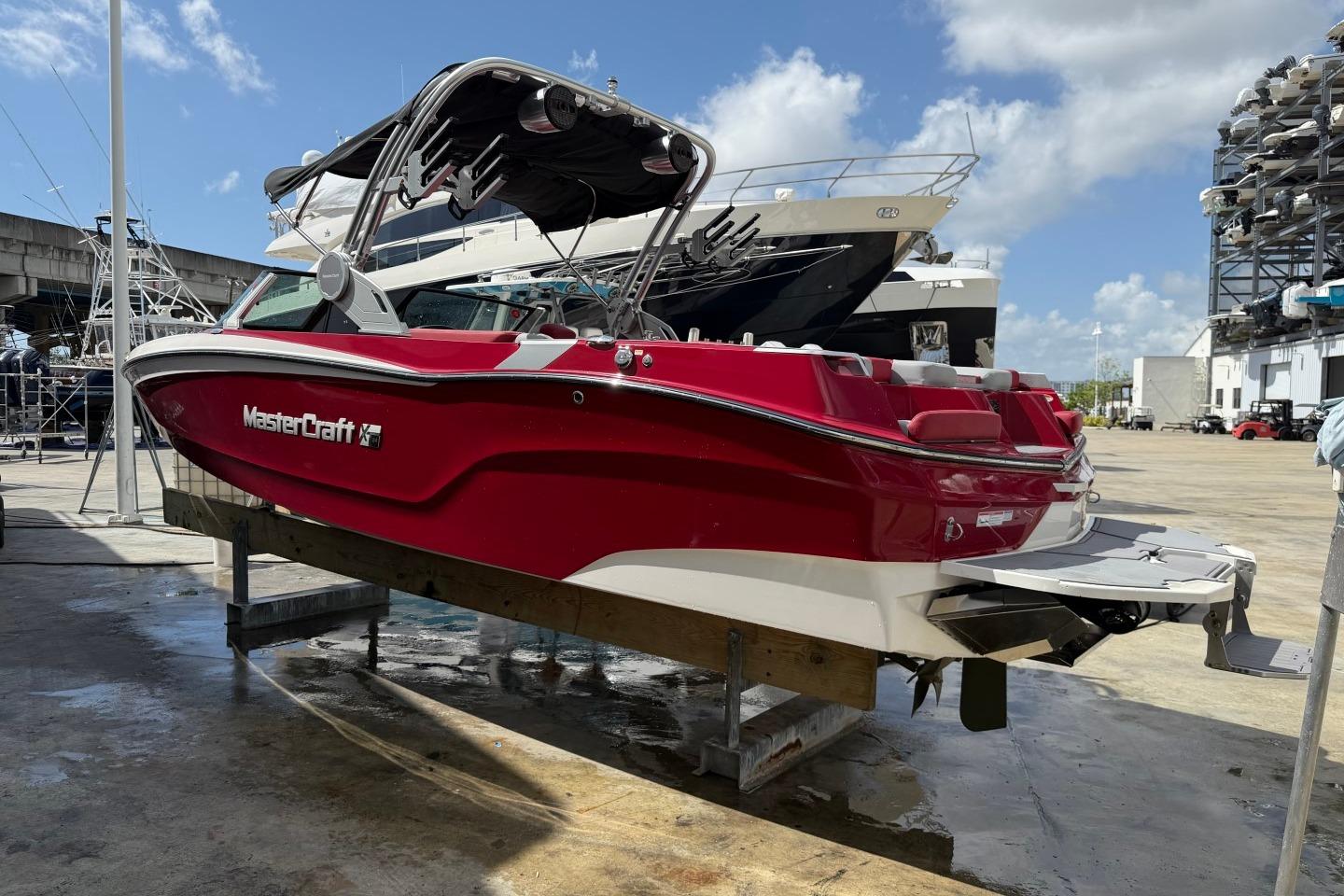 2023 MasterCraft X24 boat in vibrant red, docked at a marina under a clear blue sky.