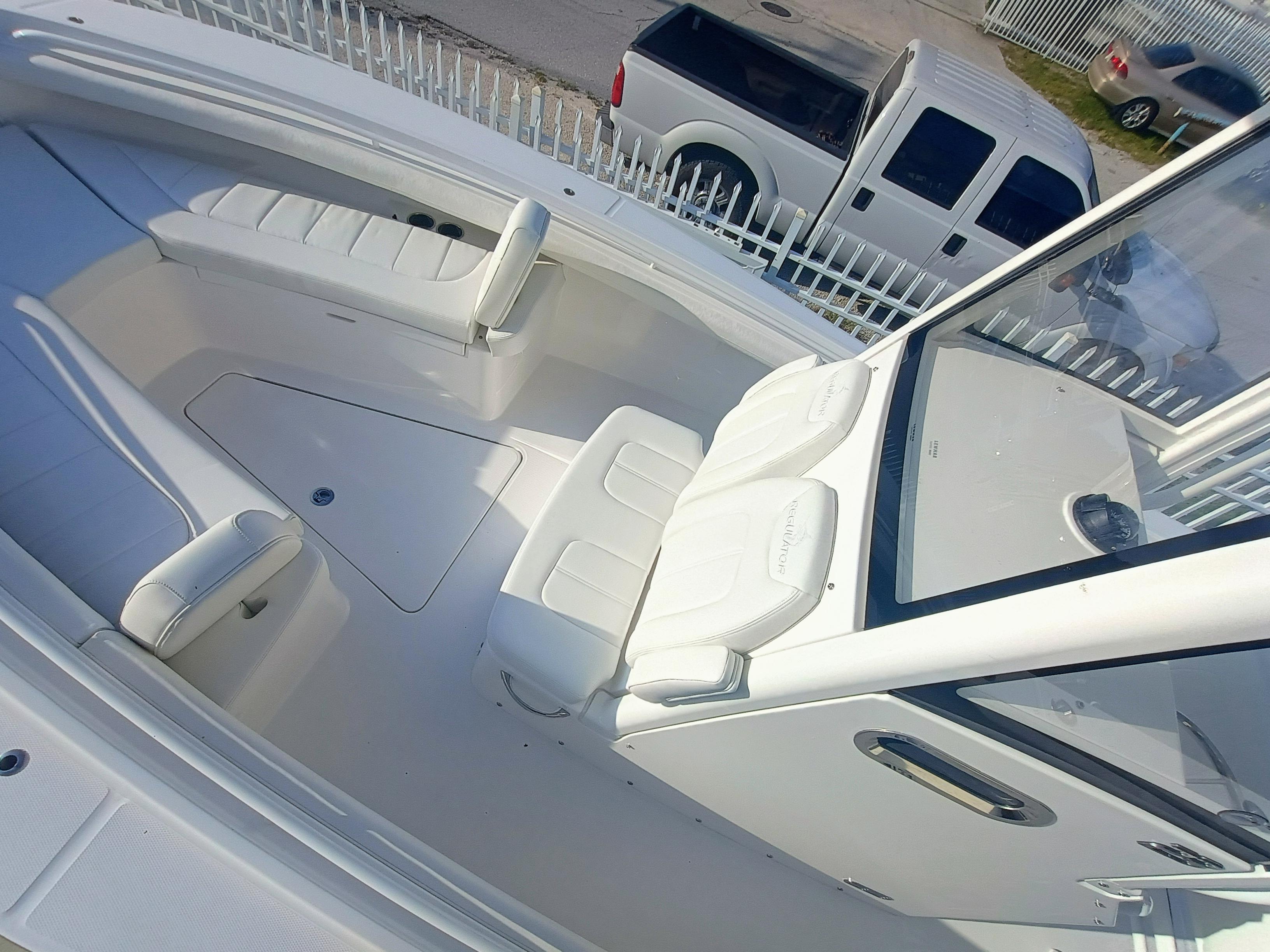 2025 Regulator 23 boat interior with white seating and console, parked near vehicles.