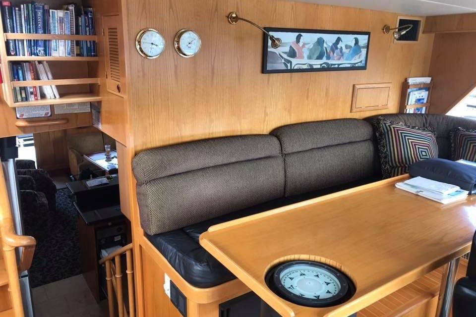 Interior of 1999 Grand Alaskan Pilothouse with cozy seating, wooden table, and nautical decor.