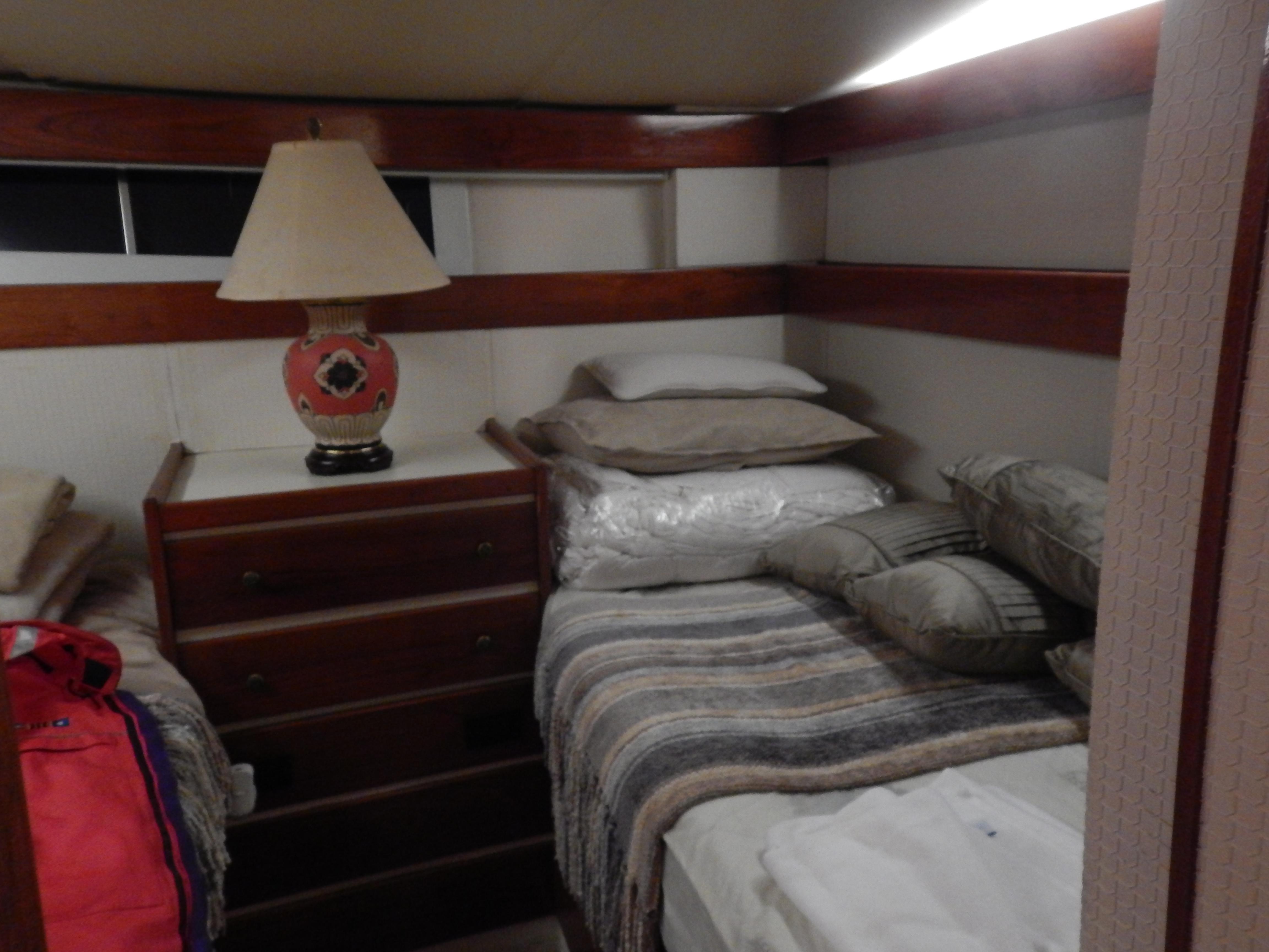 1974 Pacemaker Cockpit Motoryacht cabin with twin beds, wooden dresser, and decorative lamp.