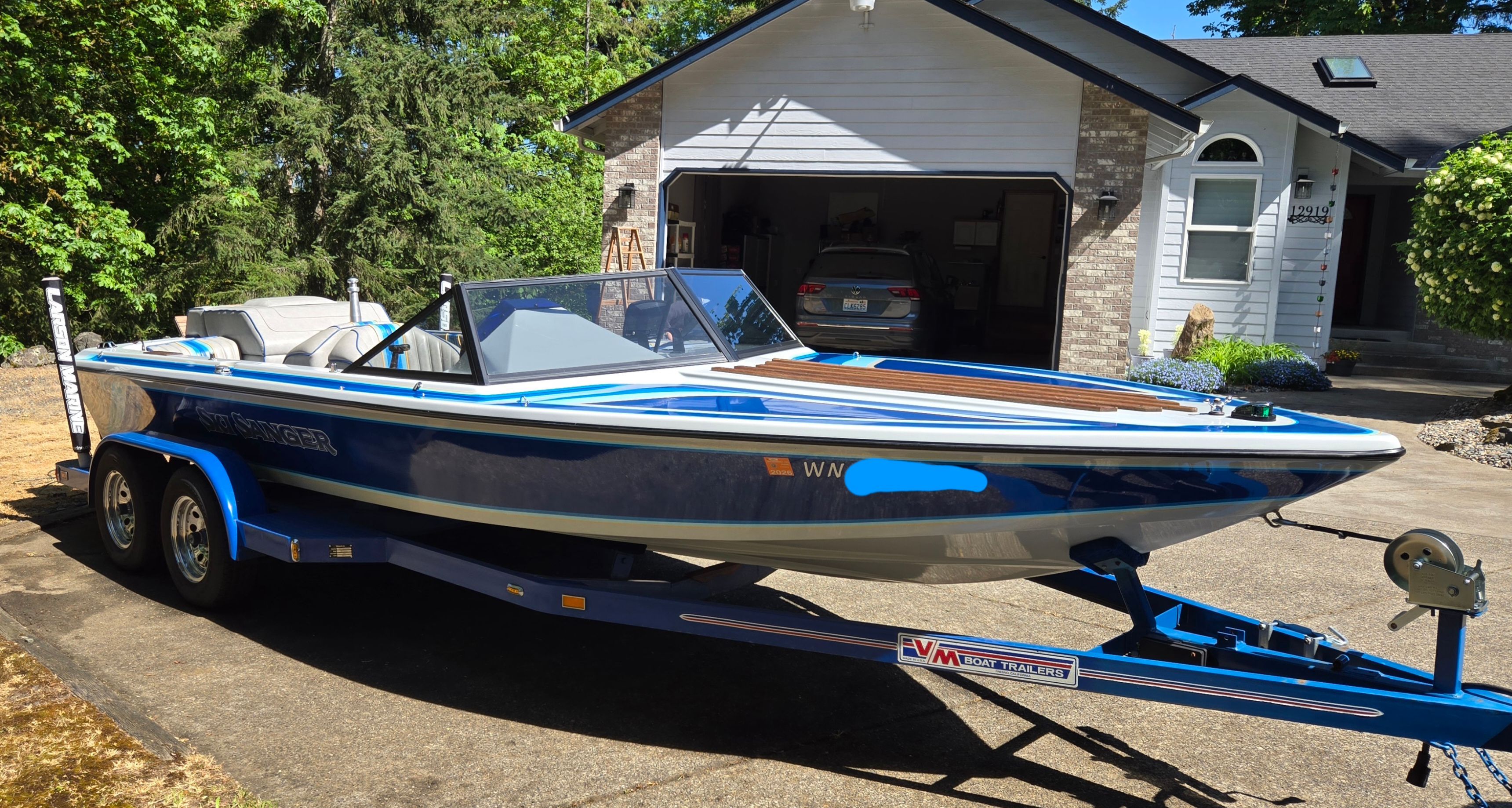 A blue 1990 Ski Sanger on a trailer in front of a house.