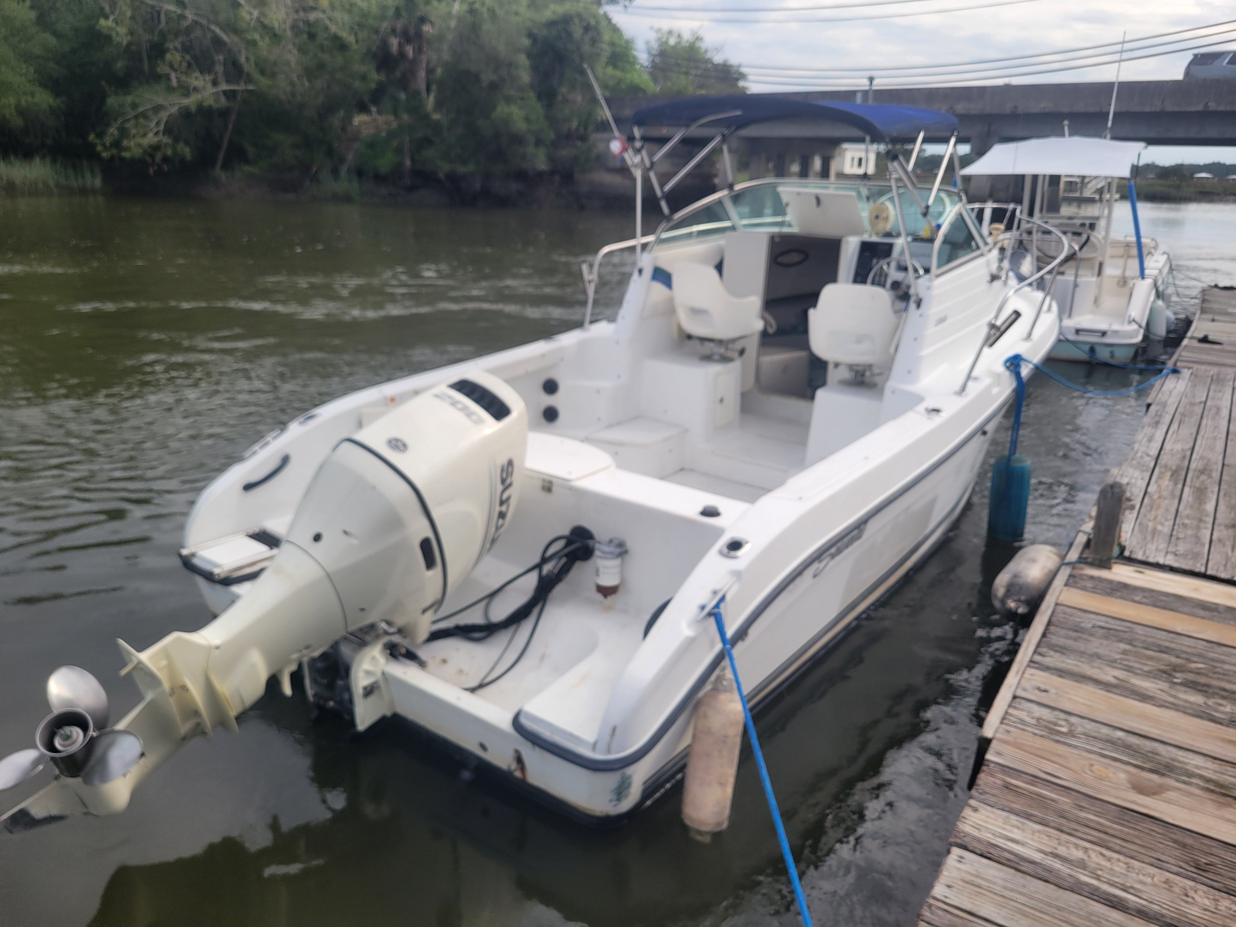 A white motorboat is docked at a wooden pier, surrounded by calm water.