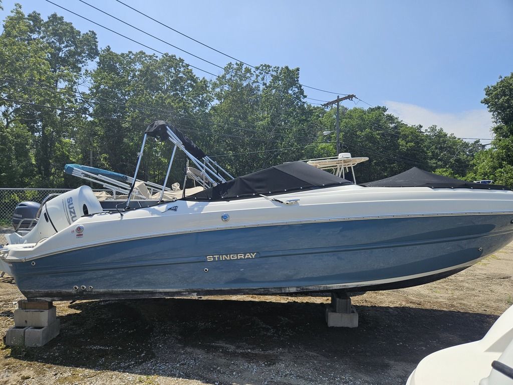 A blue and white boat is on blocks on land, surrounded by trees.