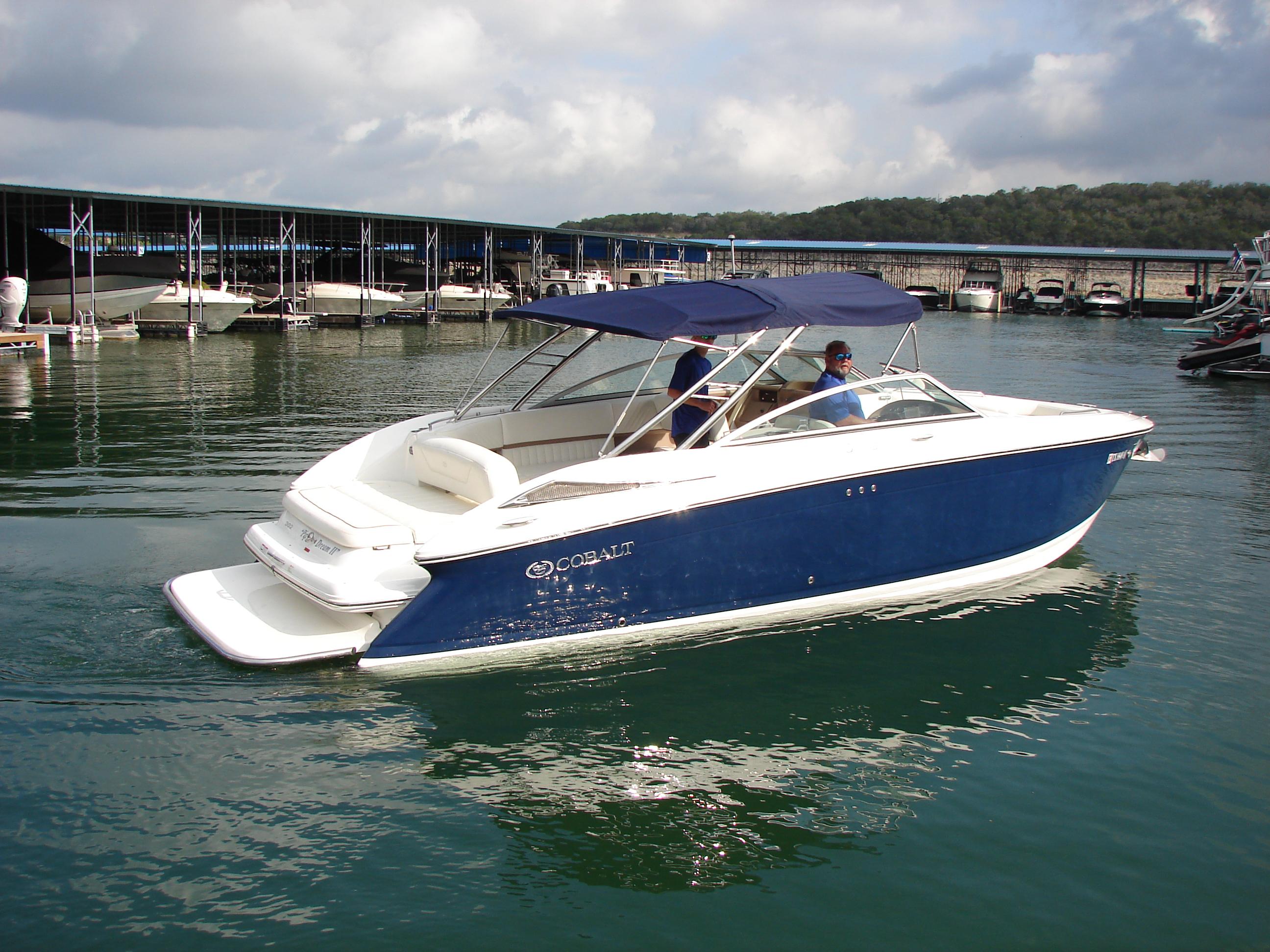 2007 Cobalt 302 boat on calm water near a marina, featuring a blue and white design.